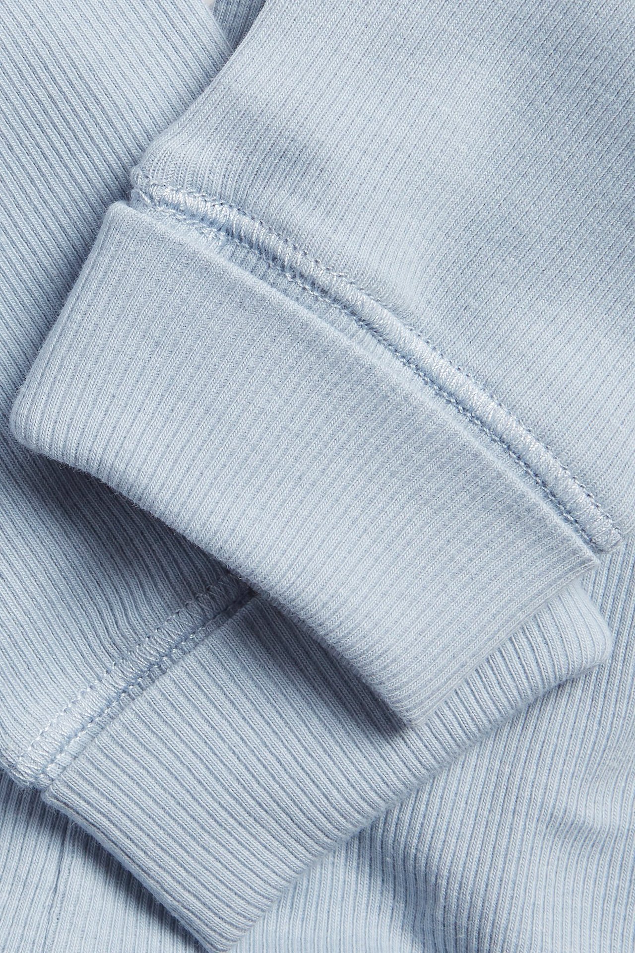 Zbliżenie na jasnoniebieskie prążkowane legginsy niemowlęce z szerokim ściągaczem na zakończeniu nogawki.