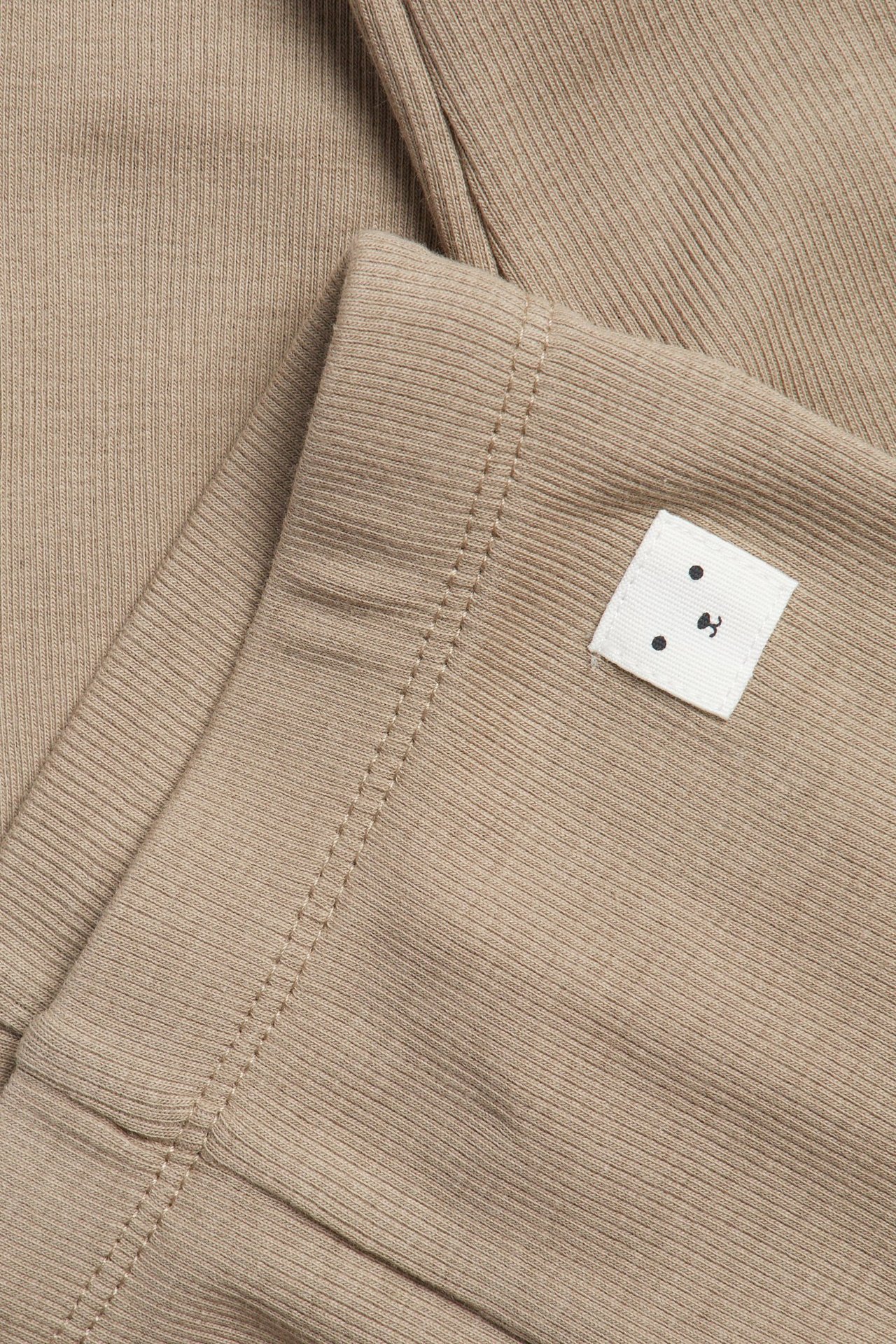 Närbild av bruna ribbade baby leggings med en liten vit etikett med björnansikte.