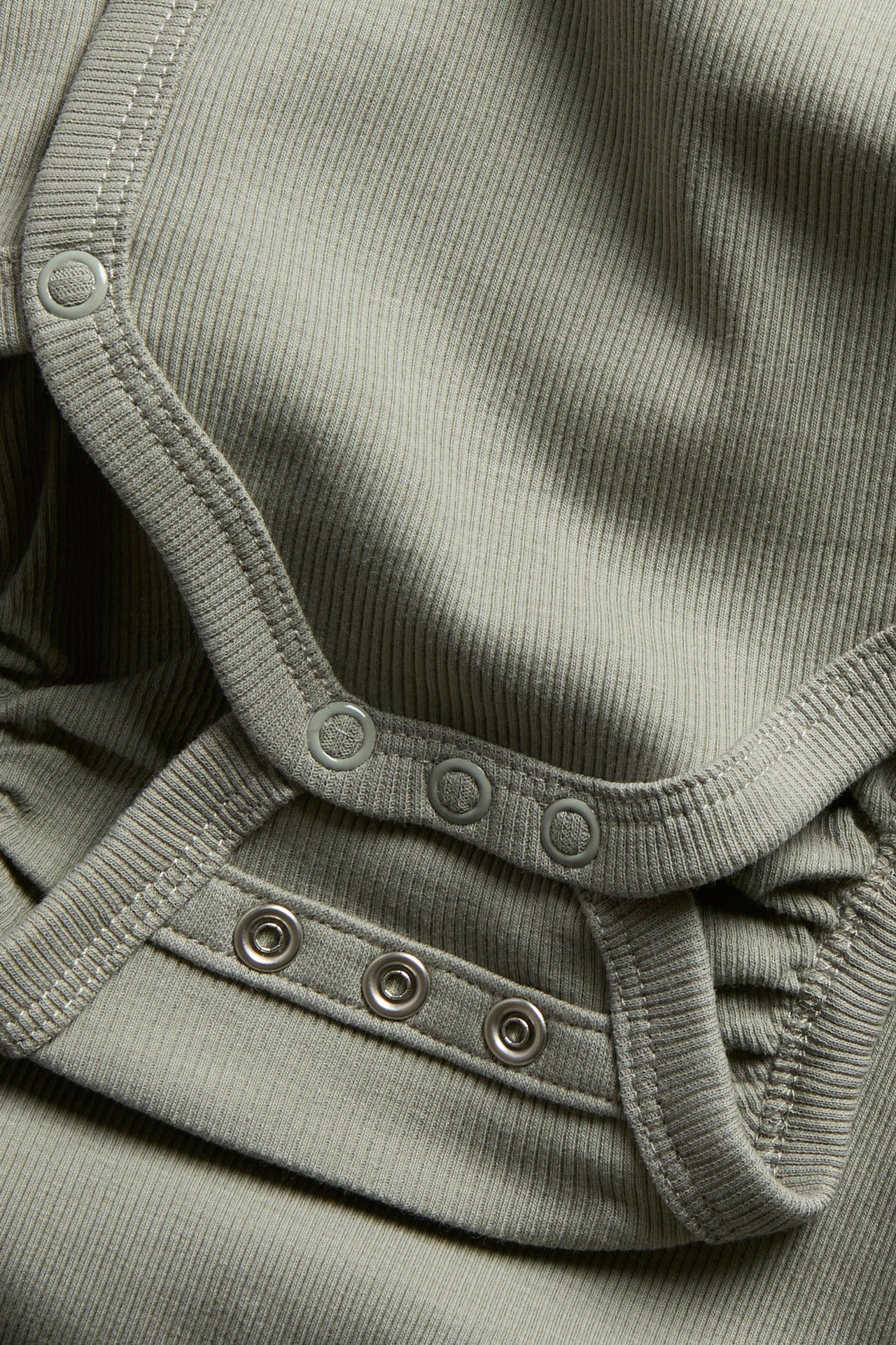 Närbild av en mörkgrön ribbad babybody med tryckknappar vid axeln och i grenen.