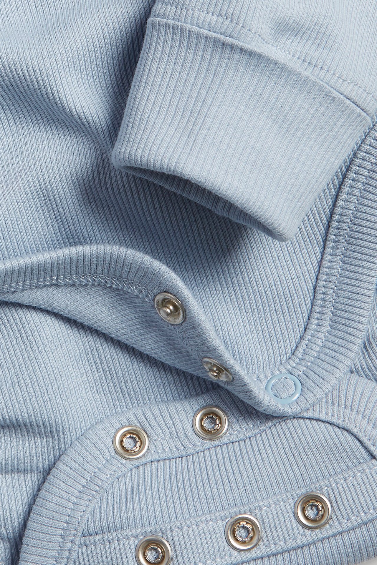 Zbliżenie na jasnoniebieskie prążkowane body niemowlęce, widoczne zatrzaski i mankiet rękawa.