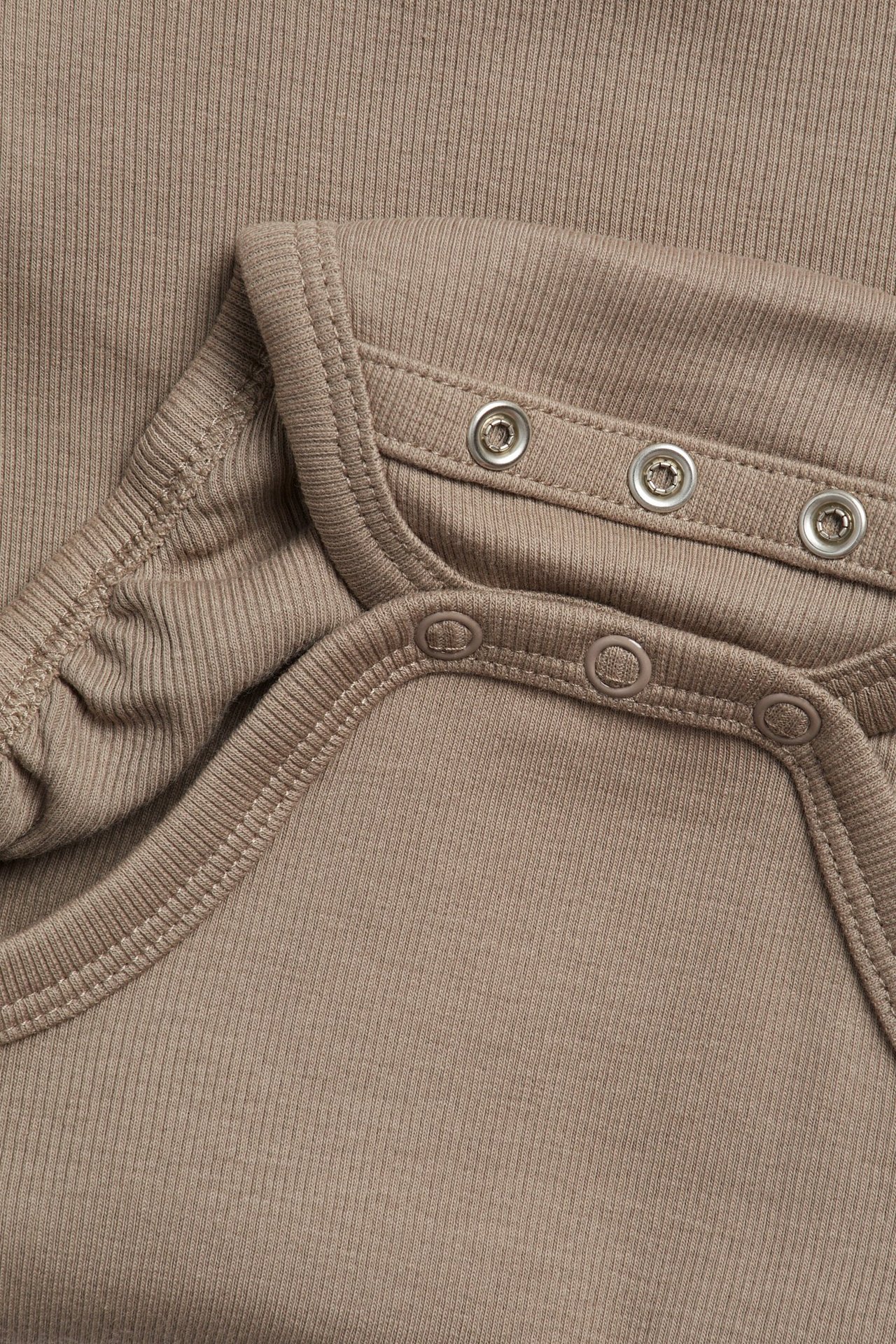 Zbliżenie brązowego, prążkowanego body niemowlęcego z zapięciem na zatrzaski.