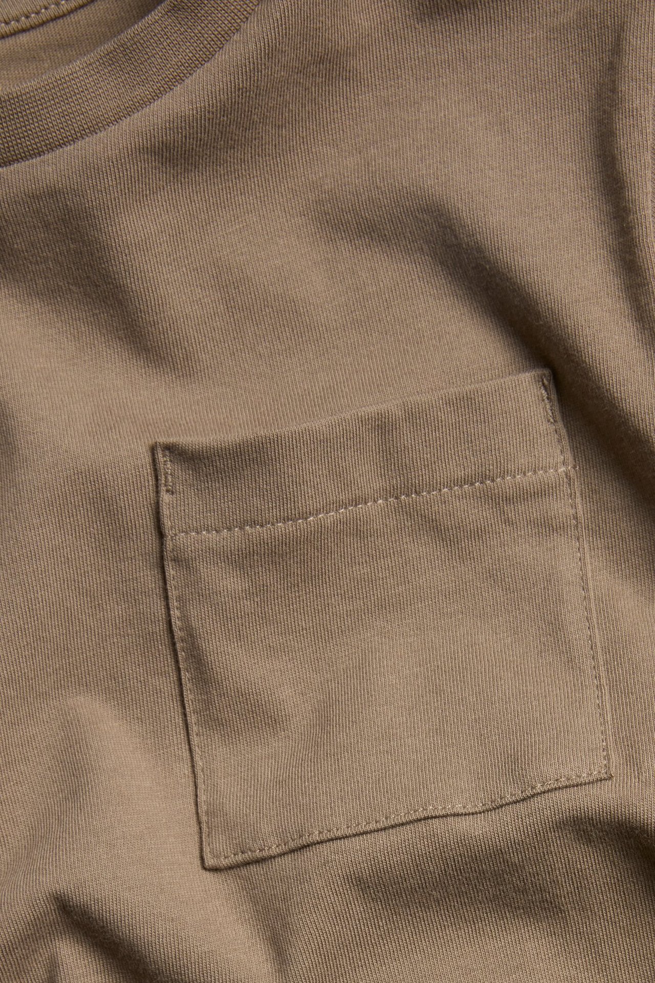 Zbliżenie na brązowy bawełniany T-shirt z długim rękawem, prążkowanym dekoltem i kieszenią na piersi.