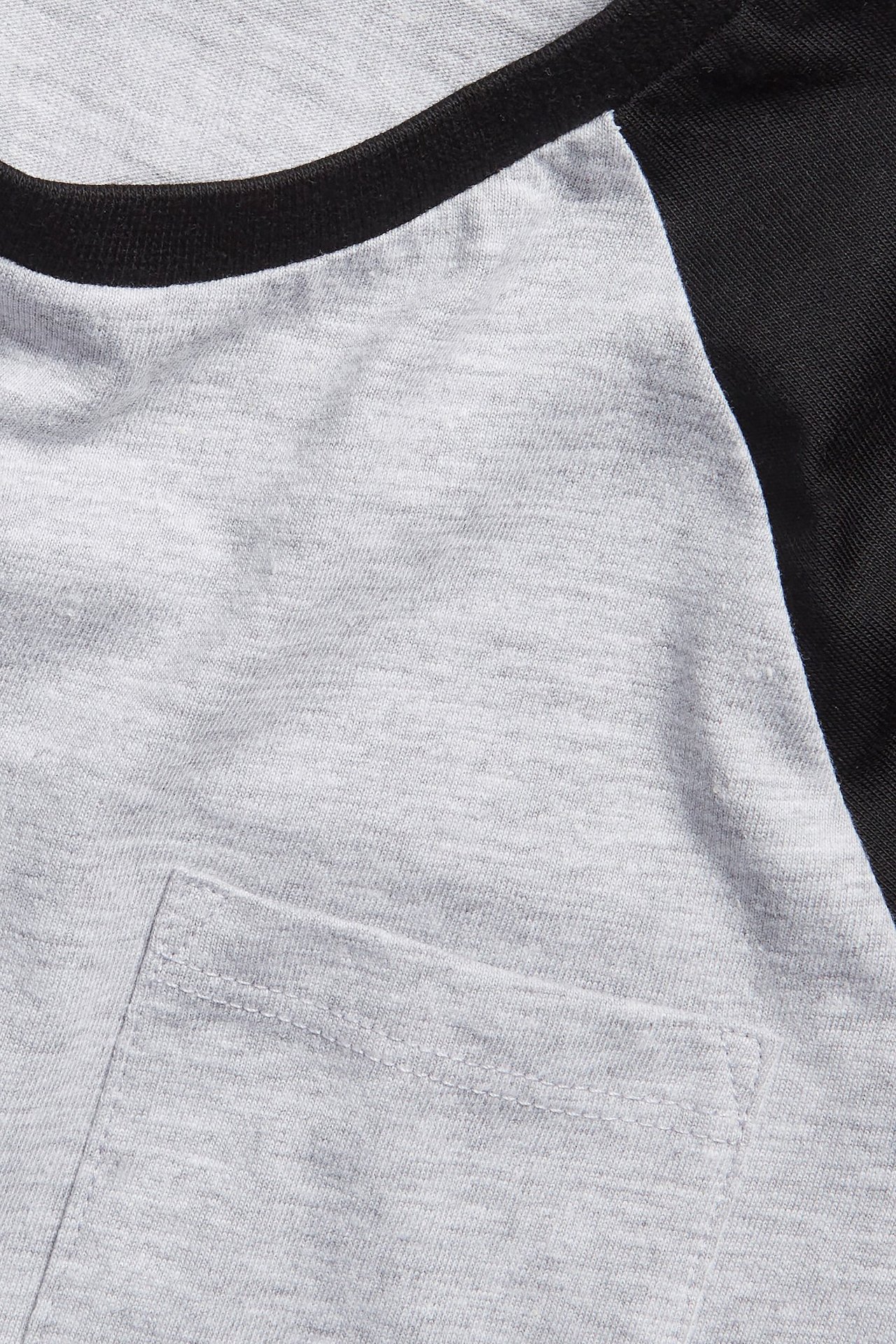 Zbliżenie na szary dziecięcy T-shirt z długim rękawem, czarnymi rękawami raglanowymi, prążkowanym dekoltem i kieszonką.