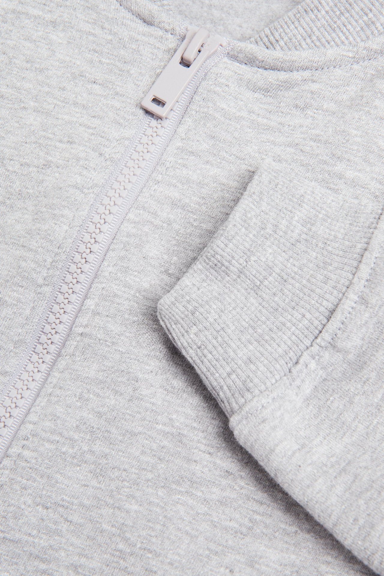 Zbliżenie jasnoszarego melanżowego kardiganu z jasnoszarym zamkiem błyskawicznym i prążkowanym mankietem.