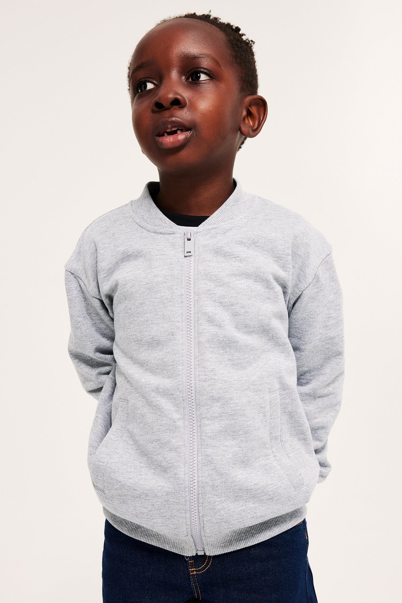 Widok z przodu dziecka w jasnoszarym melanżowym kardiganie z zamkiem błyskawicznym i ciemnoniebieskich dżinsach.