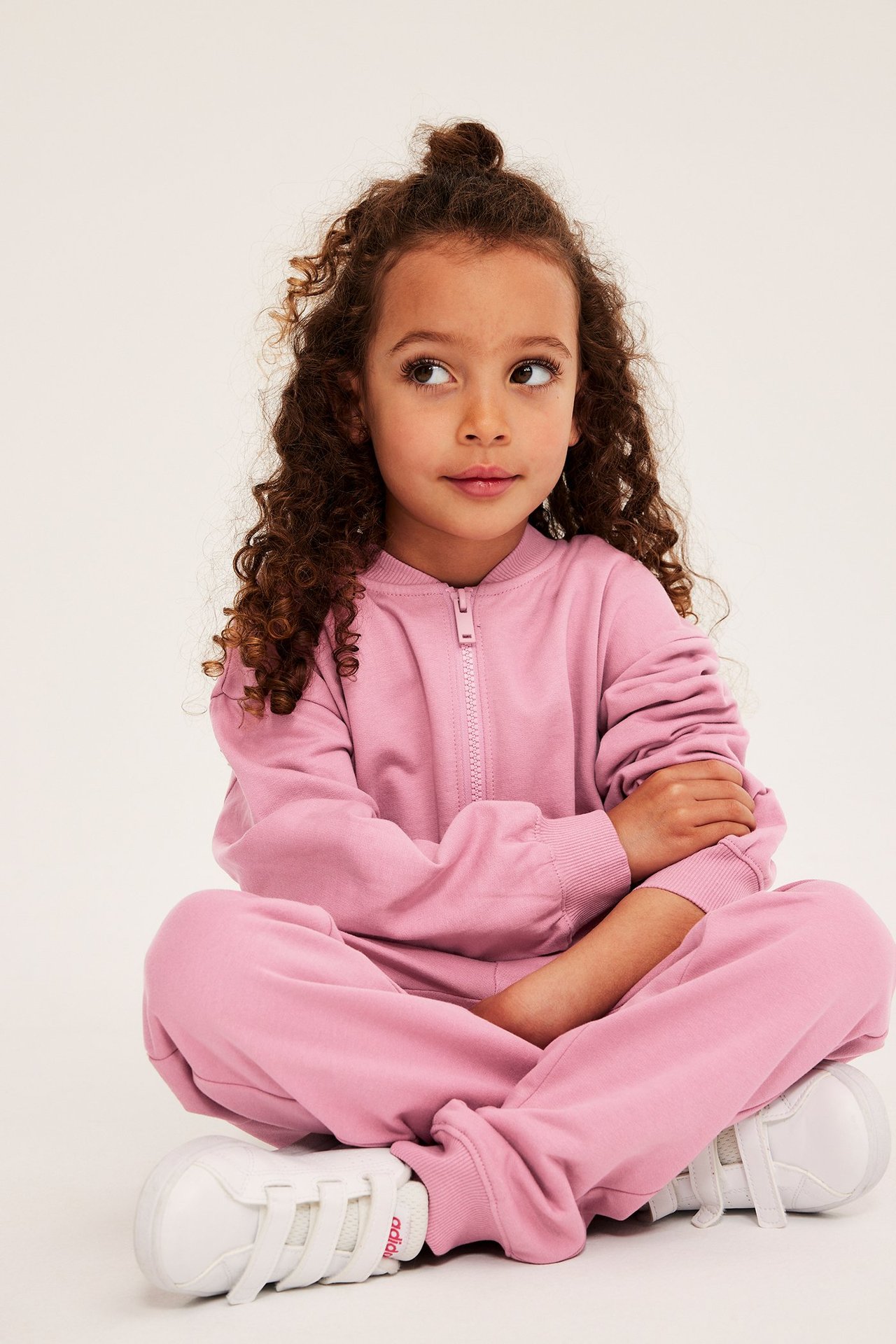 Edestäpäin: lapsi yllään vaaleanpunainen puuvillainen vetoketjullinen neuletakki, yhteensopivat collegehousut ja valkoiset lenkkarit.