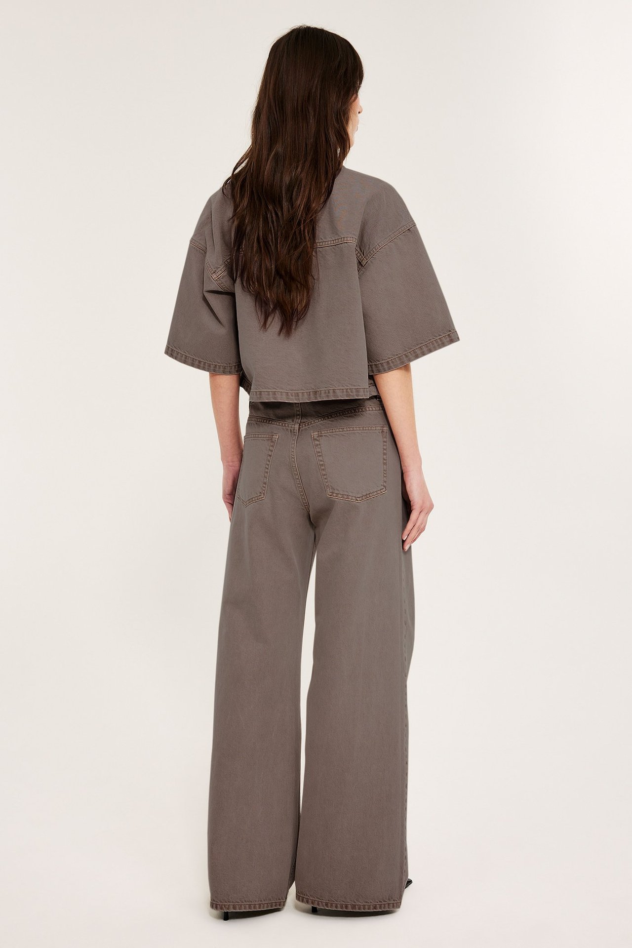 Naisen takaa näkymä vaaleanruskeissa, leveälahkeisissa, korkeavyötäröisissä farkuissa ja yhteensopivassa lyhyessä topissa.