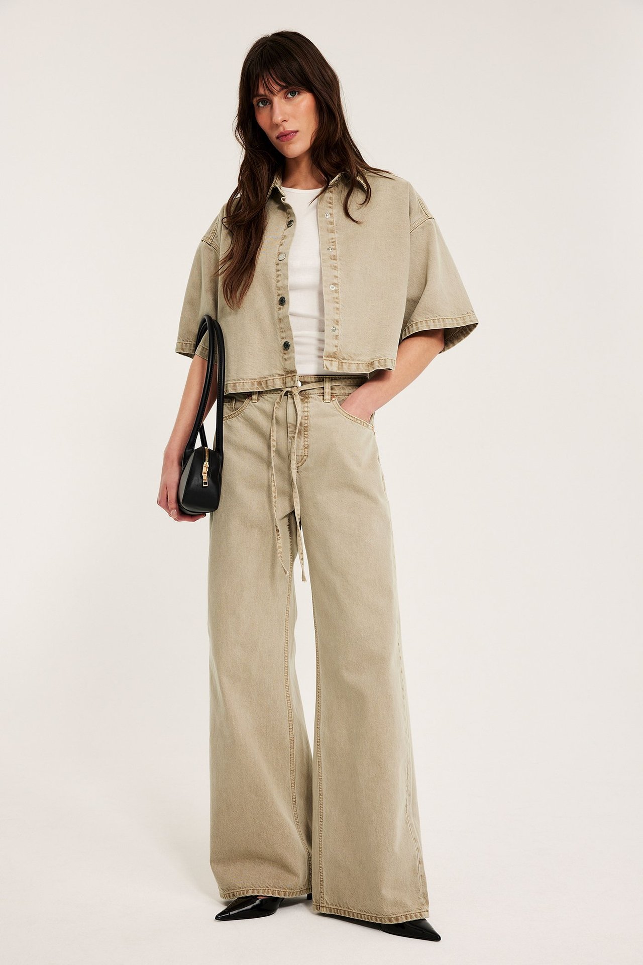Widok z przodu: Kobieta w jasnobrązowych szerokich jeansach z paskiem, pasującej krótkiej koszuli i białym topie.