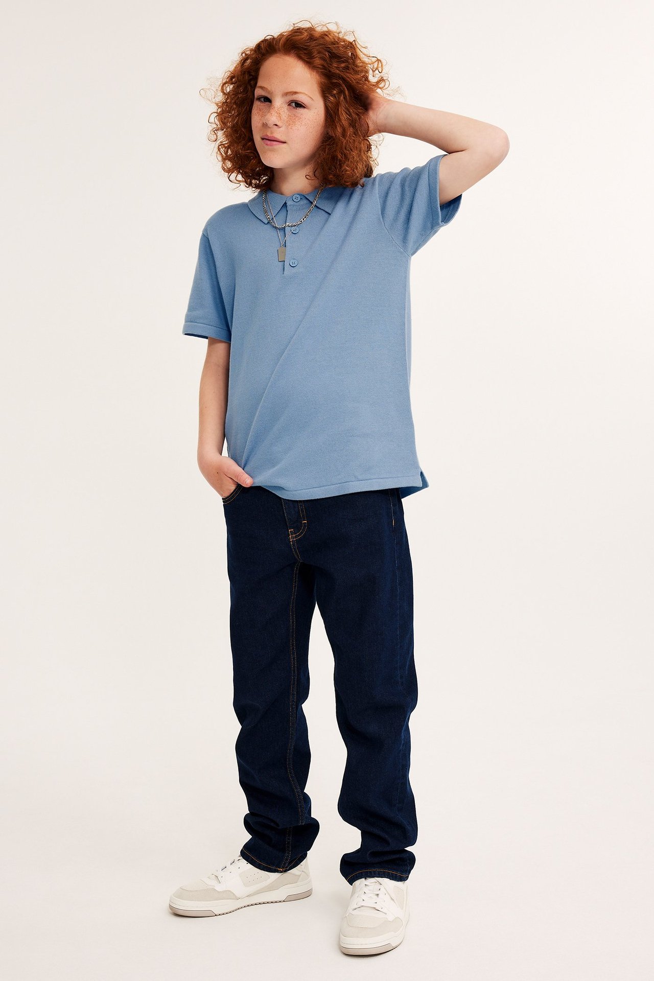 Dziecko z przodu: jasnoniebieska bawełniana koszulka polo, ciemnoniebieskie dżinsy, białe trampki.