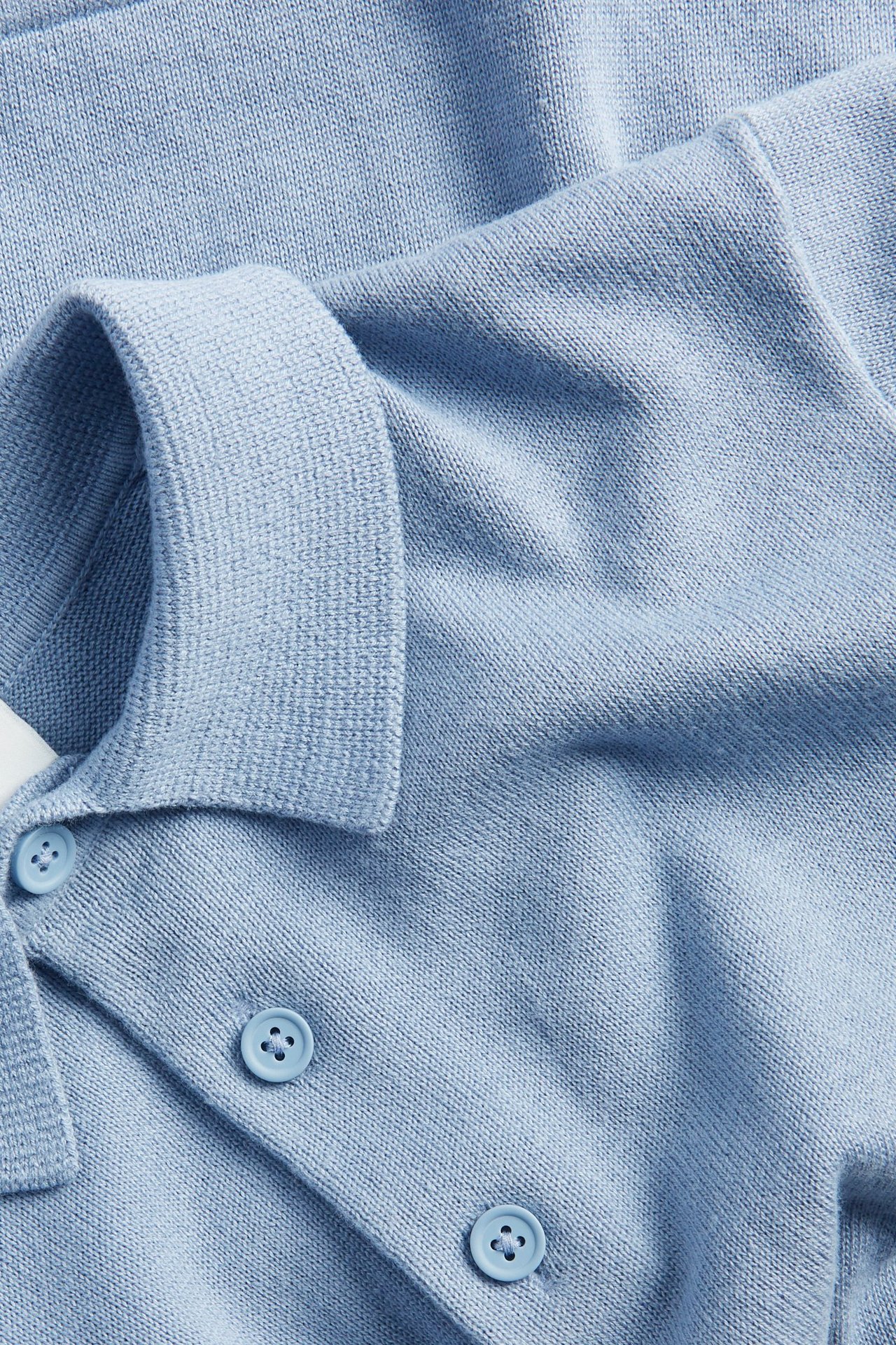 Zbliżenie na jasnoniebieską, drobno dzianą koszulkę polo z bawełny, z kołnierzykiem i trzema guzikami.