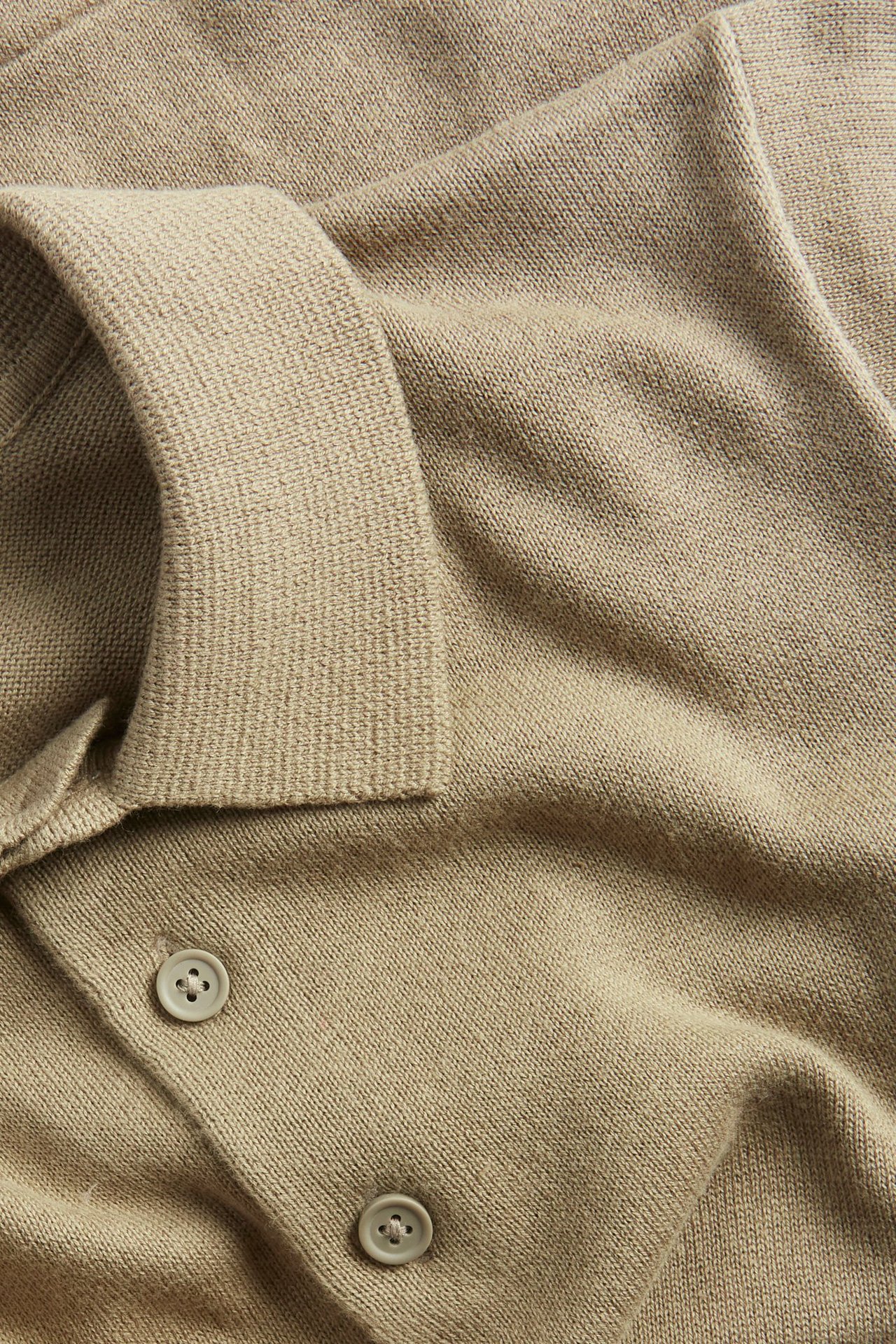 Zbliżenie na ciemnobeżową, drobno dzianą koszulkę polo z bawełny, z kołnierzykiem i dwoma guzikami.