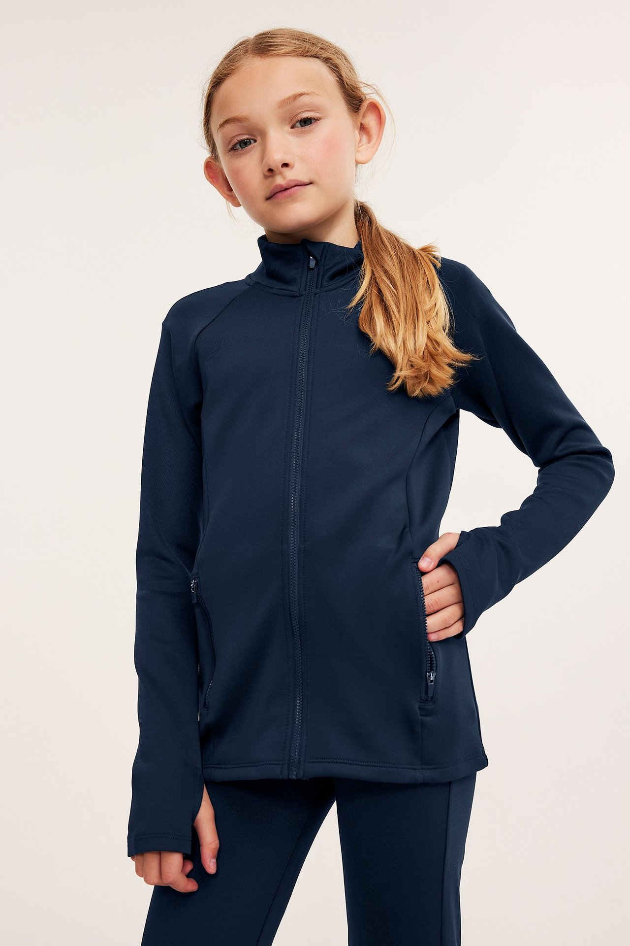 Edestä, lapsi tummansinisessä vetoketjullisessa treenitakissa, jossa pystykaulus ja yhteensopivat housut.