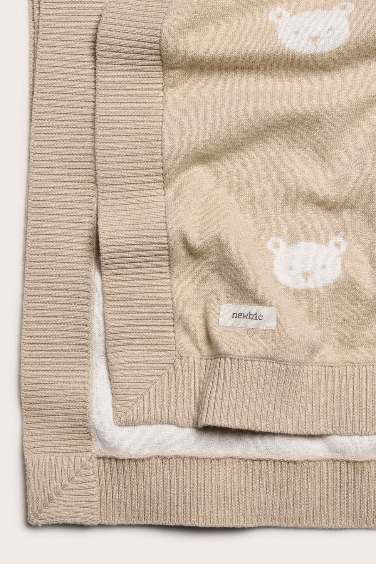 Närbild på en beige jacquardstickad bomullsfilt med vitt nallemönster, vikt för att visa baksidan.