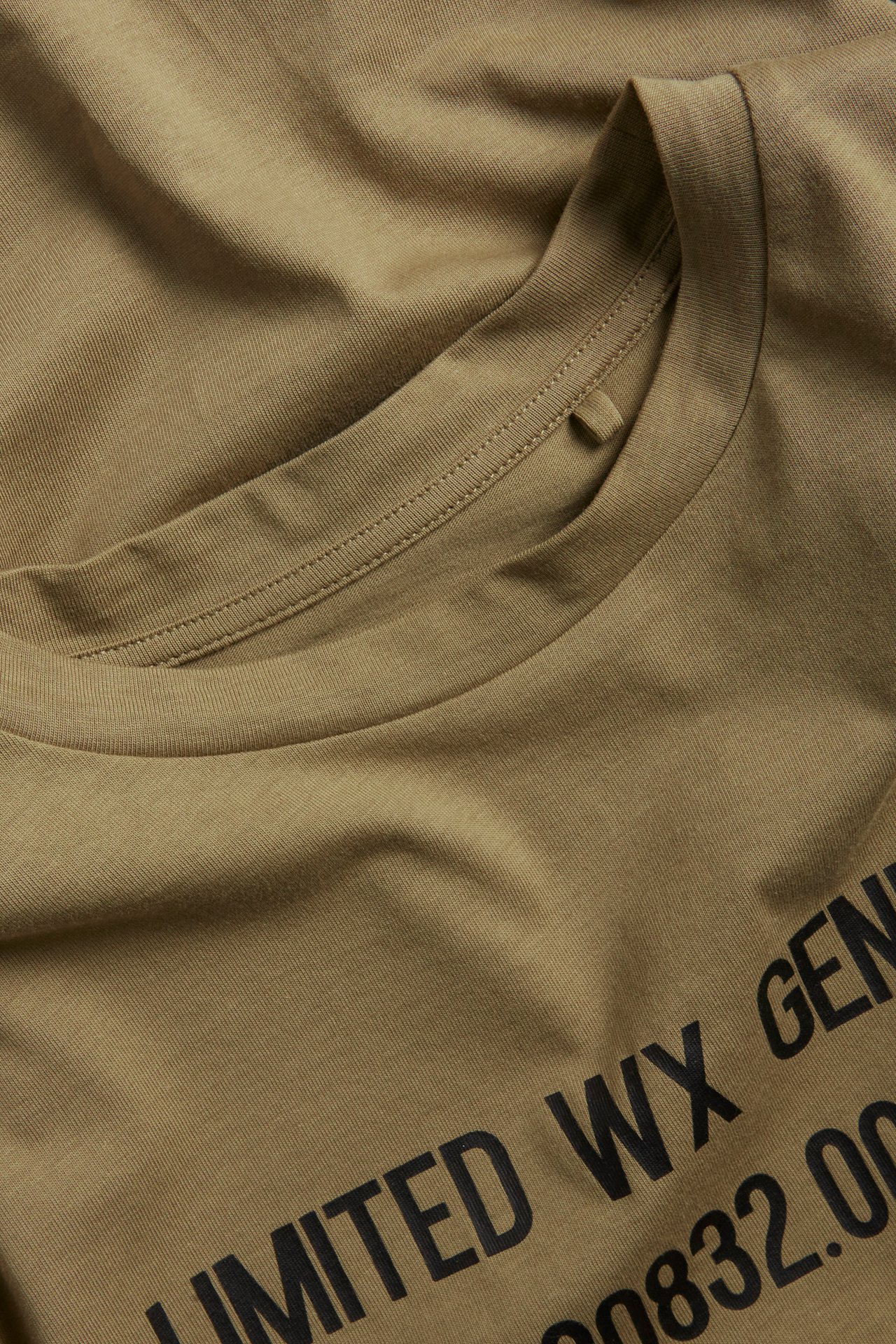 Zbliżenie na brązowy bawełniany T-shirt oversize z prążkowanym dekoltem i czarnym nadrukiem z przodu.