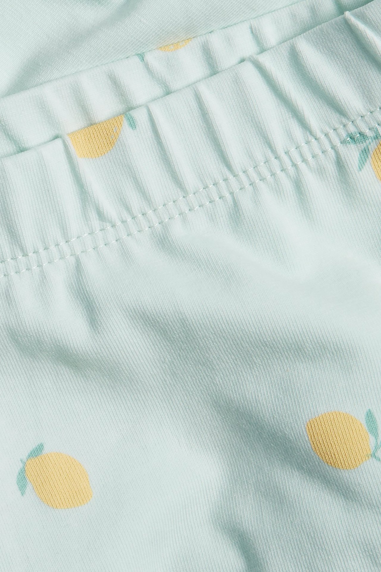 Zbliżenie na jasnozielone szorty rowerowe dziecięce z żółtym wzorem w cytryny i elastycznym pasem.