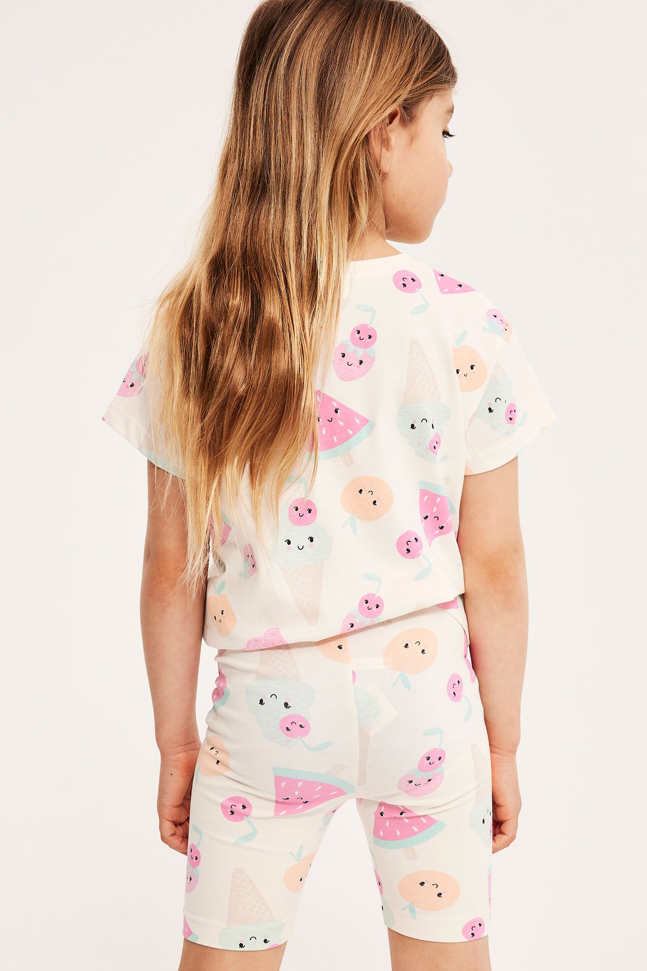 Bakifrån: ett barn i offwhite mönstrade cykelshorts och en matchande kortärmad t-shirt.