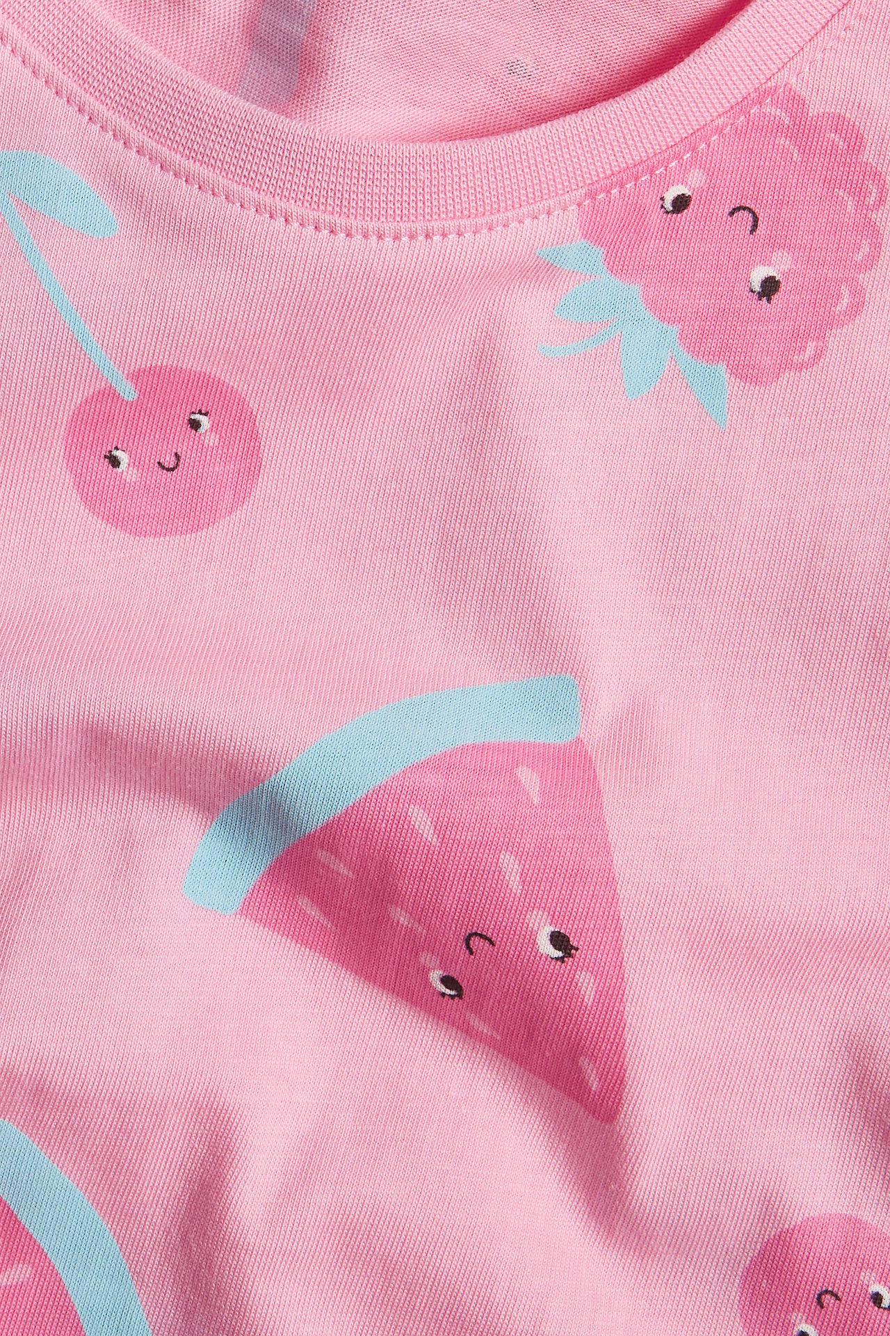 Närbild på en rosa bomulls-t-shirt för barn med frukttryck av körsbär, jordgubbar och vattenmelon.