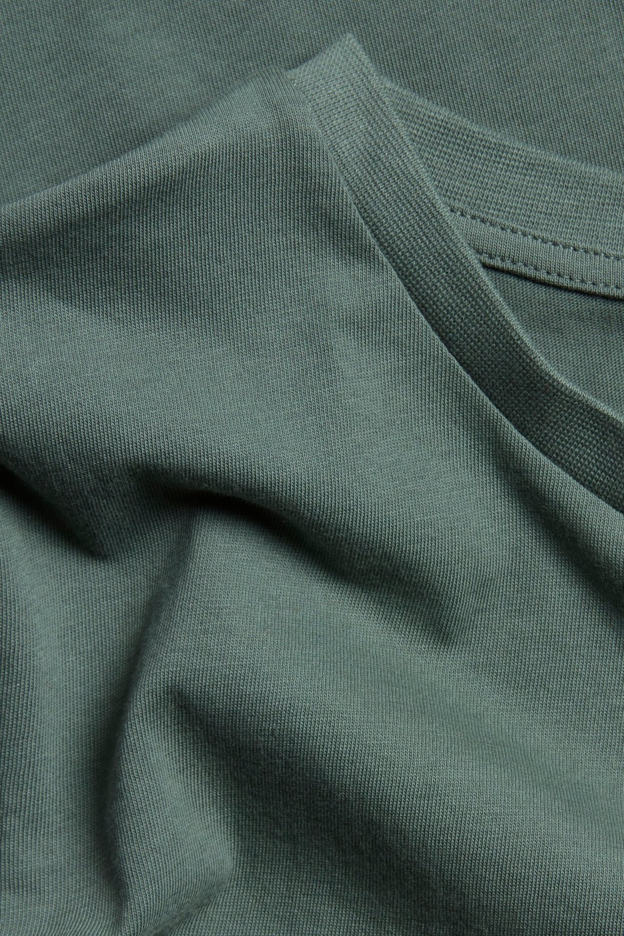 Zbliżenie na jednokolorowy, khaki zielony bawełniany t-shirt z prążkowanym dekoltem.
