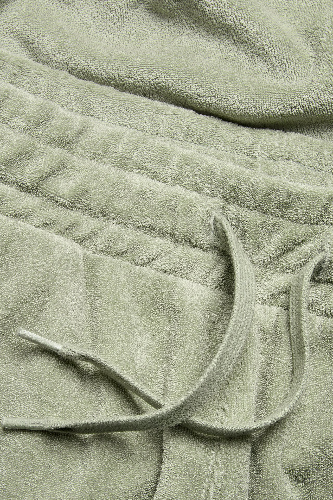 Närbild av mörkgröna frottéshorts med elastisk midja och dragsko.