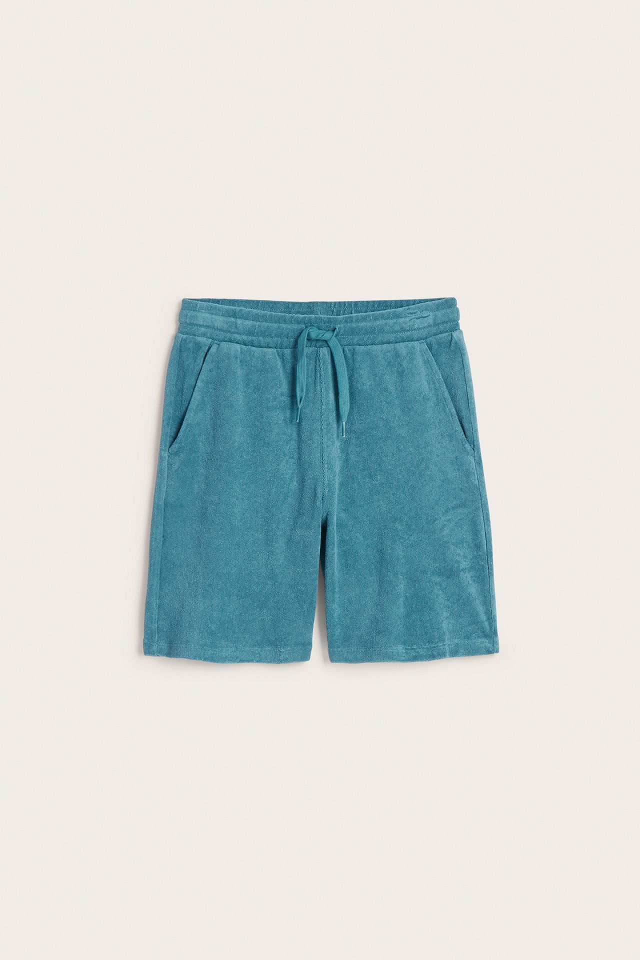Frontvisning av grønne frottéshorts for barn med elastisk midje, snøring og lommer.