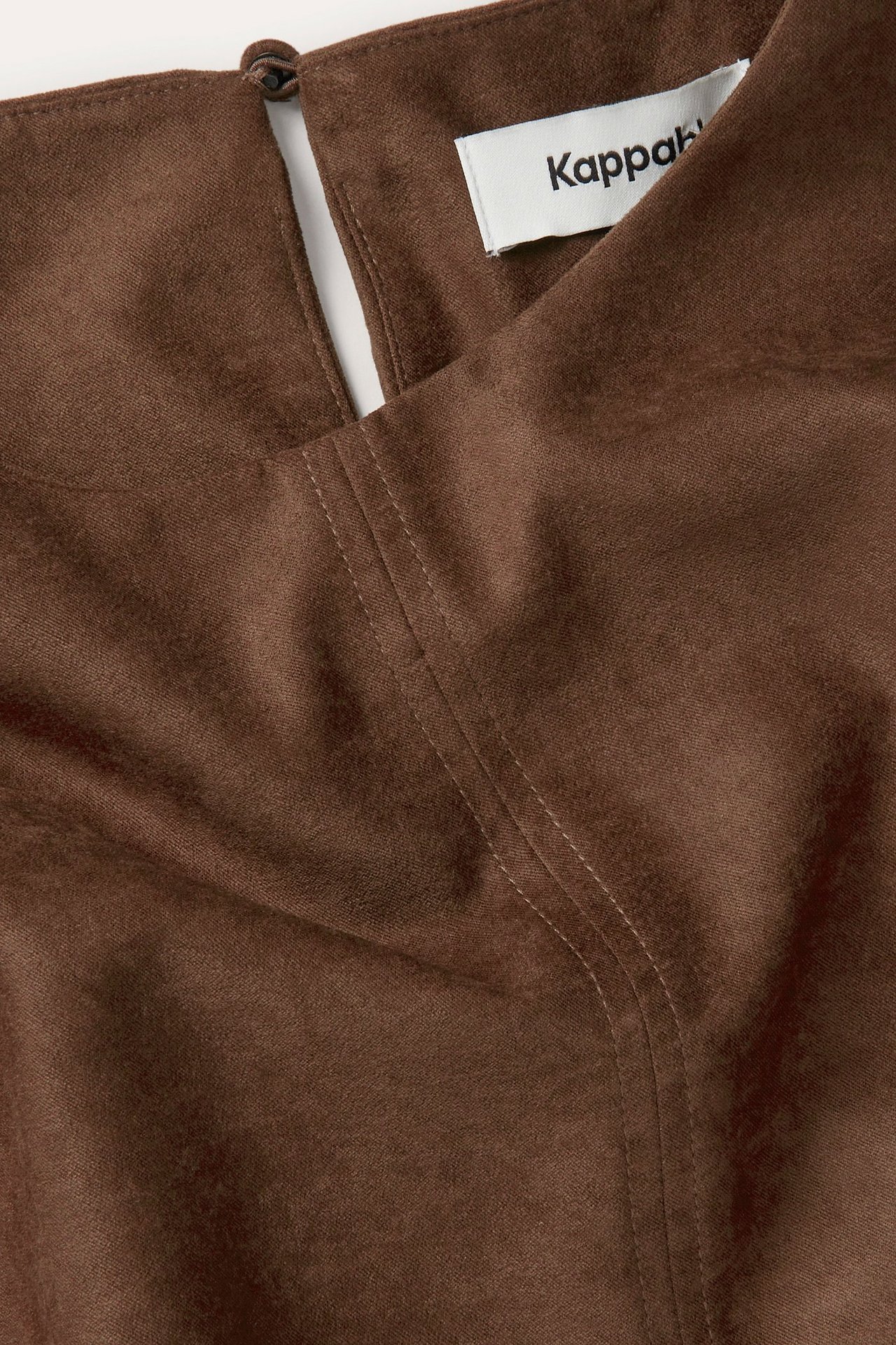 Zbliżenie brązowego, krótkiego topu z imitacji zamszu z zapięciem na guzik z tyłu i widocznymi szwami.