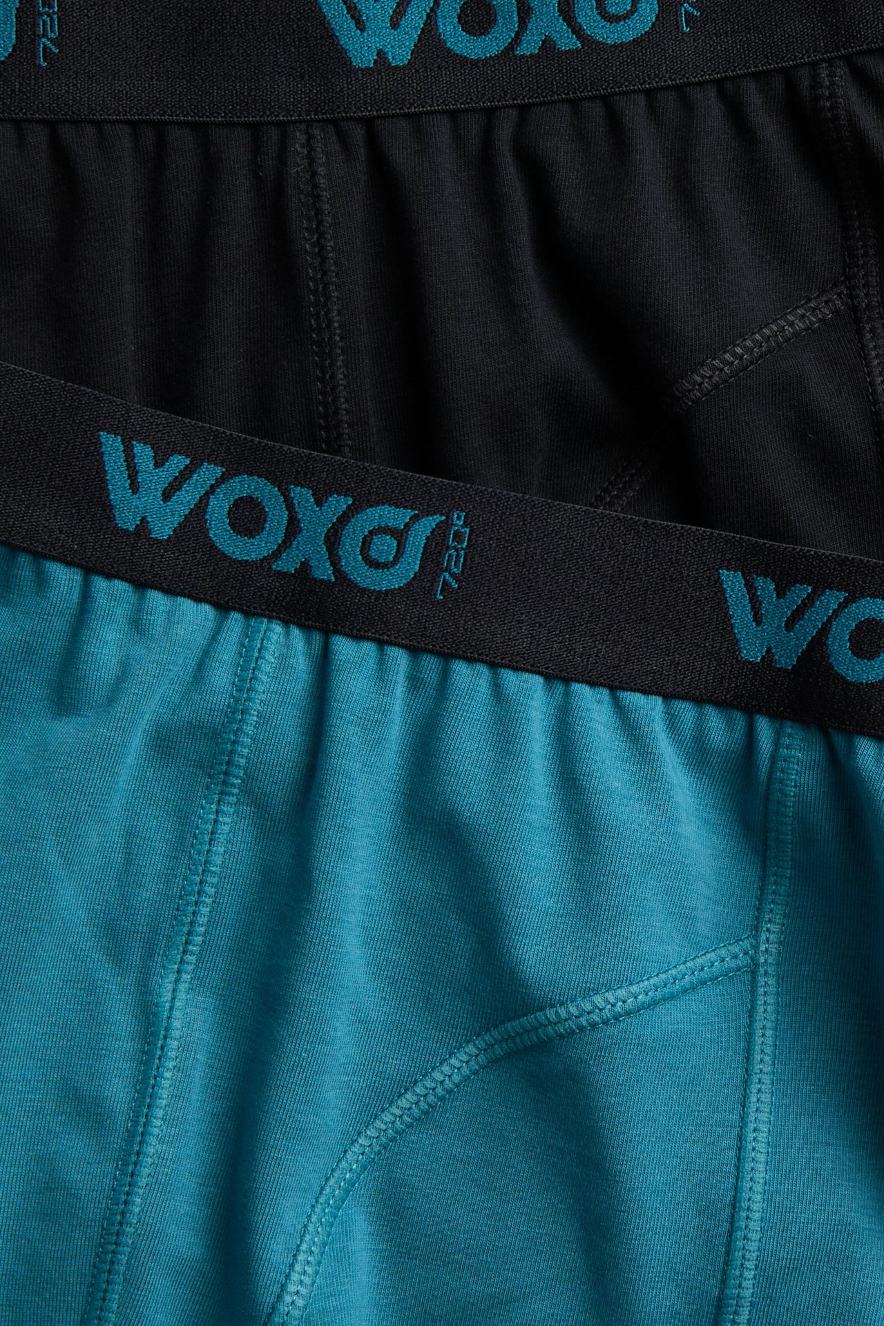 Zbliżenie na turkusowe bokserki dziecięce z czarnym pasem "WOXO" i czarną parą z tyłu.