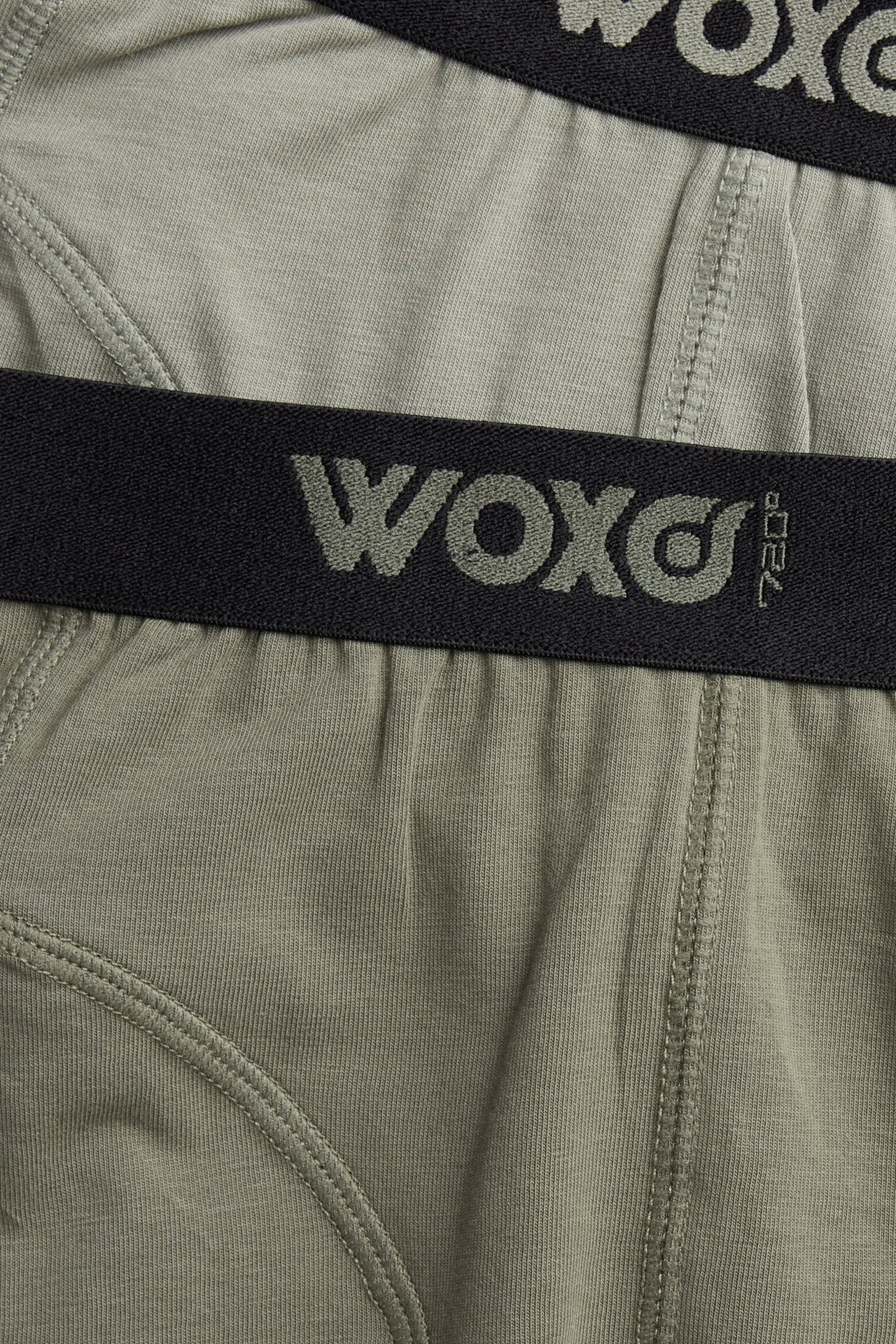 Zbliżenie na zielone, gładkie bokserki chłopięce z mieszanki bawełny, z czarnym elastycznym pasem WOXO.