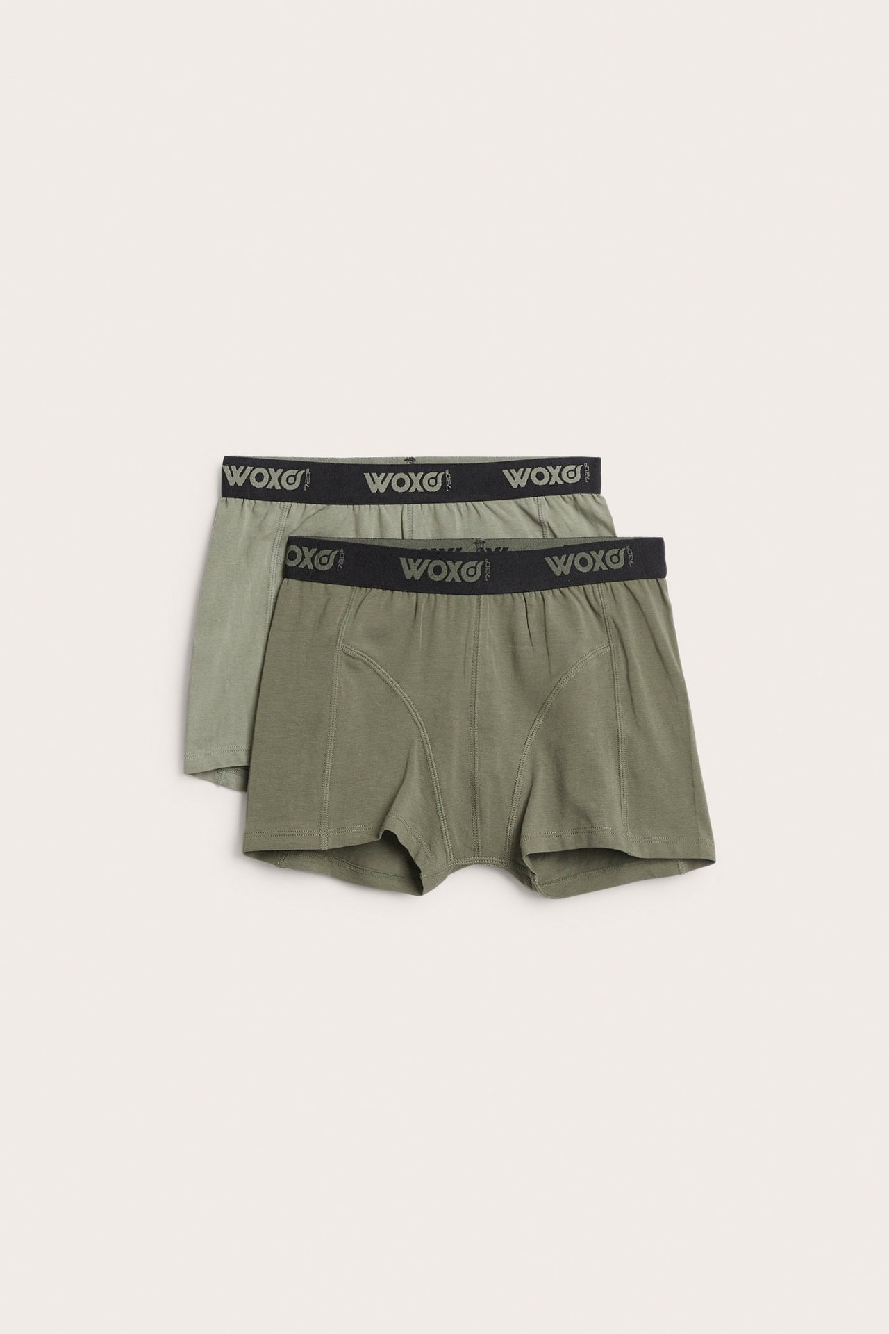 Widok z przodu dwóch par zielonych bokserek dziecięcych, jedne ciemne, drugie jasne, z pasem Woxo.