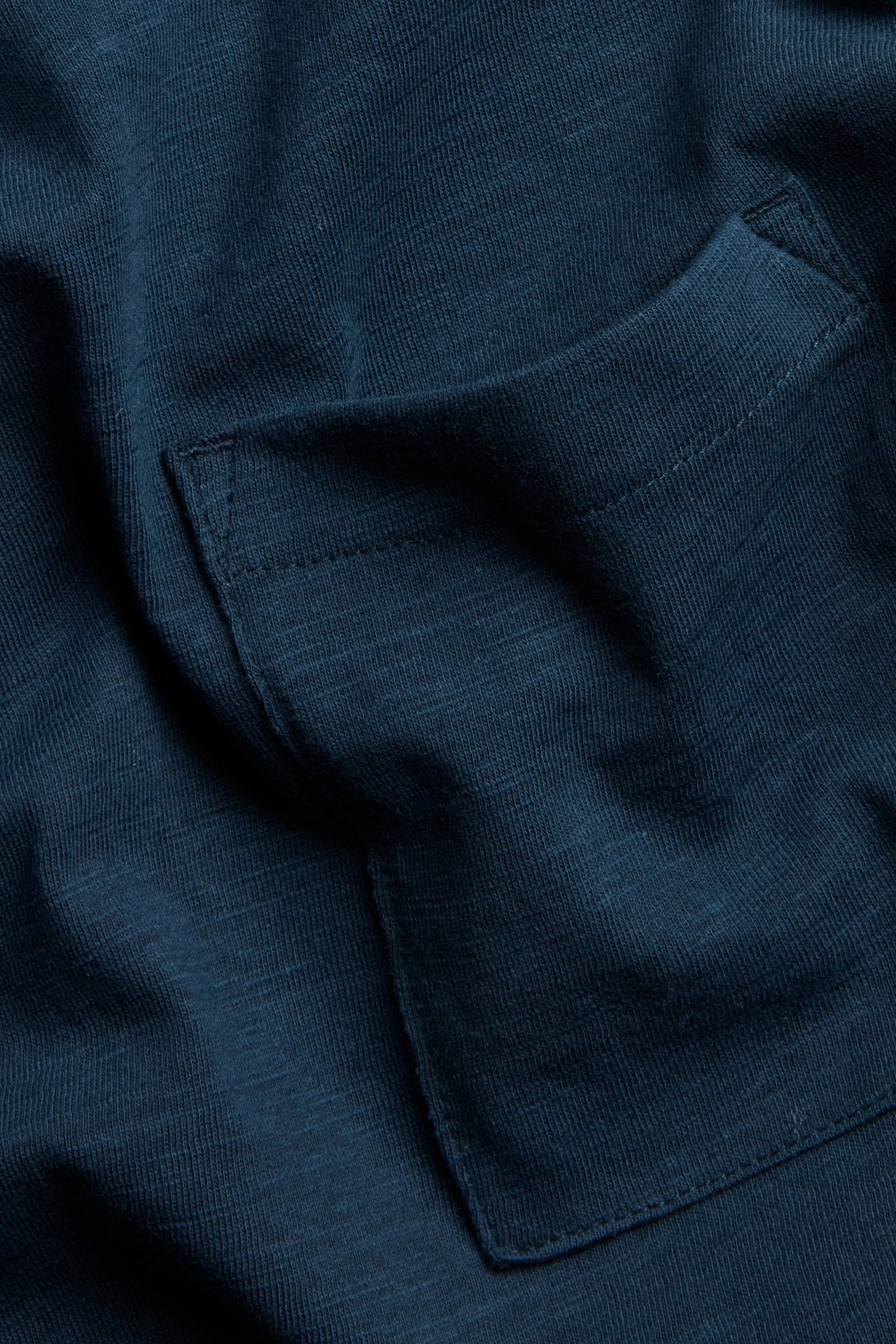 Zbliżenie na granatową koszulkę z długim rękawem z bawełny slub, z naszywaną kieszenią.