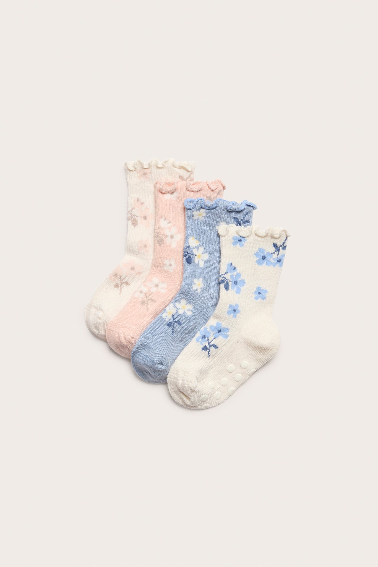 Fyra babystrumpor: ljusblå, rosa och krämfärgade med blommigt mönster, volangkanter och halkskydd.