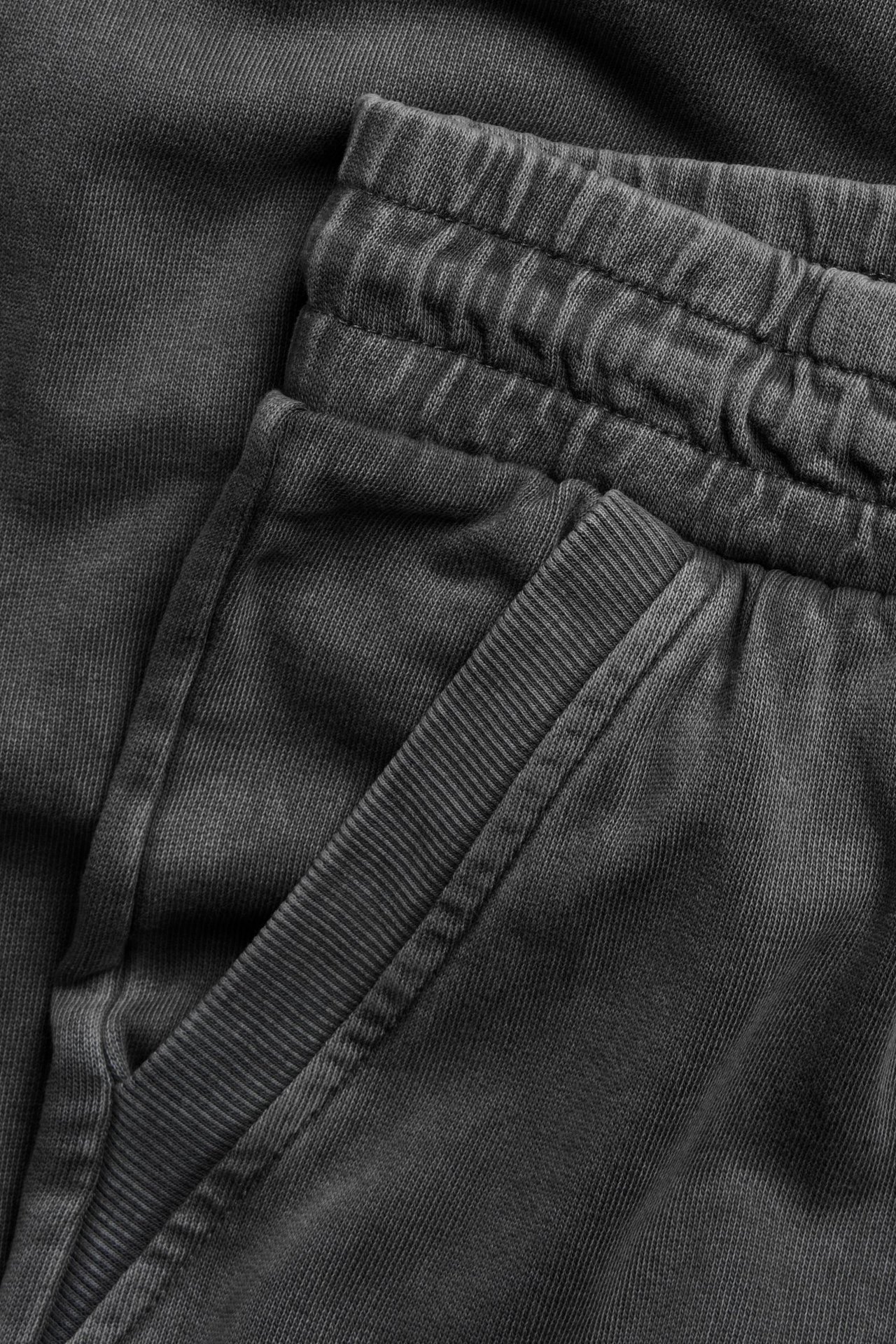 Zbliżenie na czarne bawełniane spodnie dresowe z efektem sprania, elastyczną talią i prążkowanym wykończeniem kieszeni.