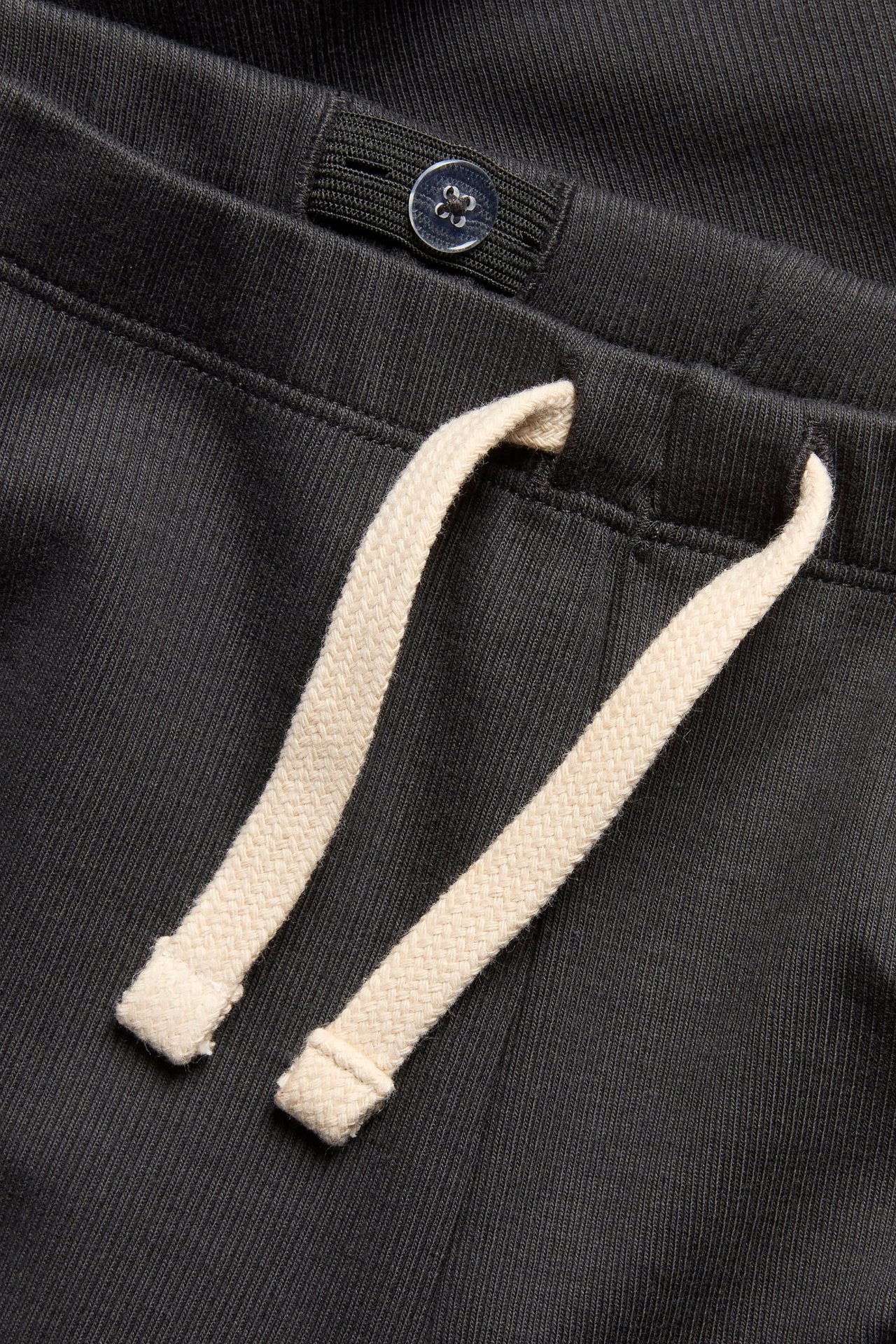 Lähikuva mustista ribbileggingseistä, joissa kermanvärinen valenauha ja säädettävä vyötärönappi.