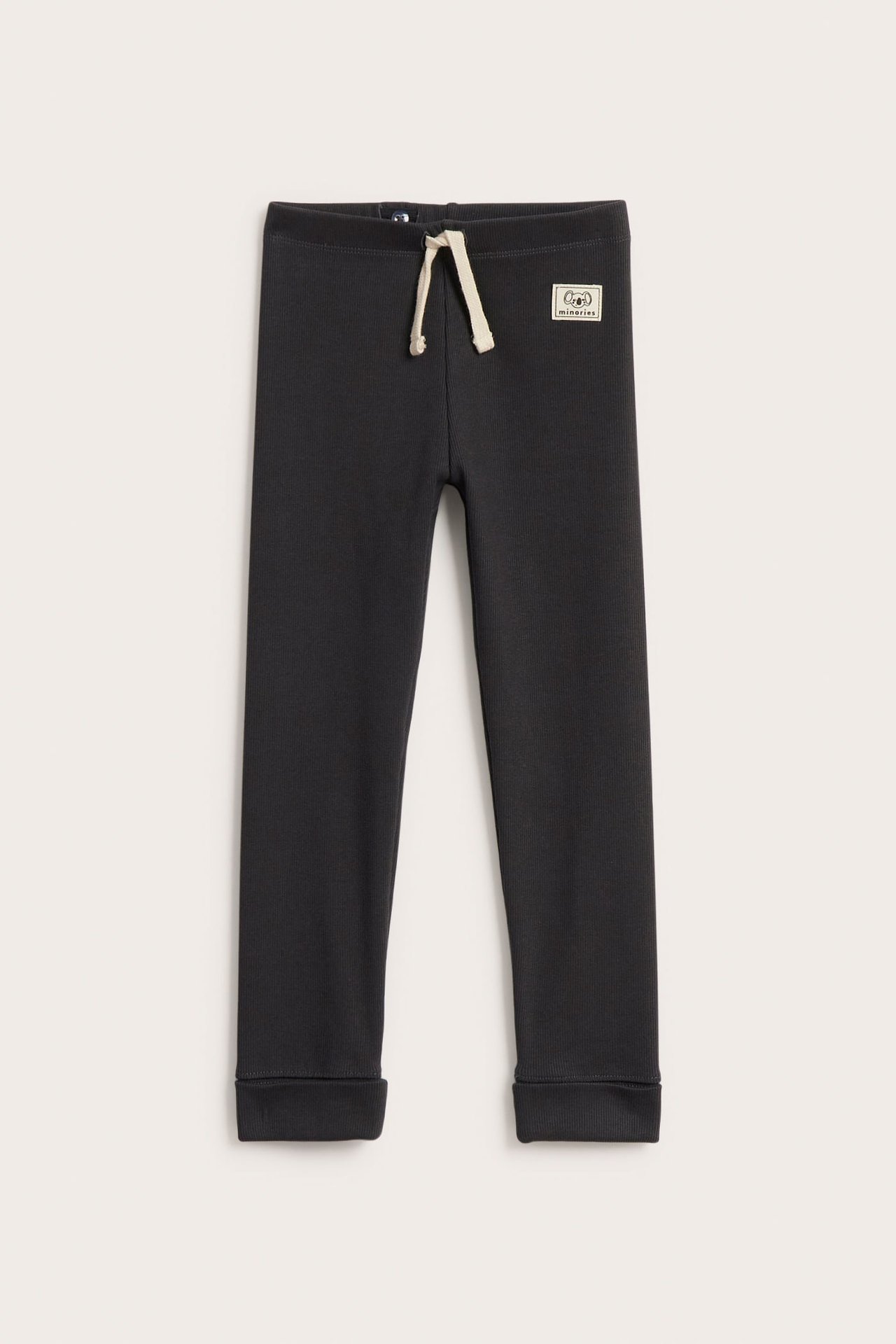Forfra svarte ribbestrikkede barneleggings med pyntesnor i midjen og nedbrettbare mansjetter.