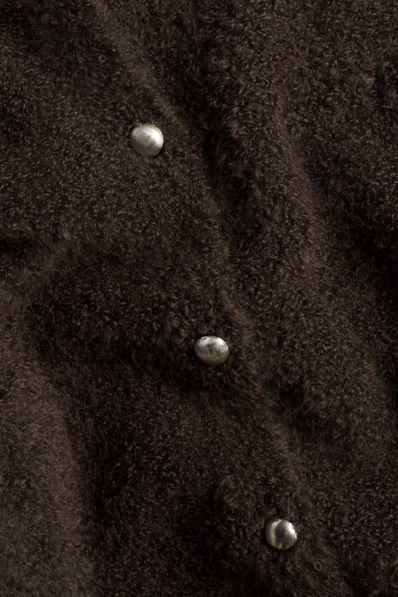 Zbliżenie brązowego, miękkiego swetra rozpinanego z okrągłymi srebrnymi guzikami.