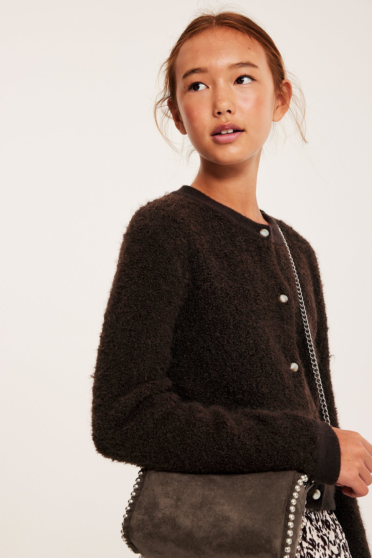 Lapsi edestä: ruskea neulekardigaani hopeanapeilla ja harmaa olkalaukku nastoilla.