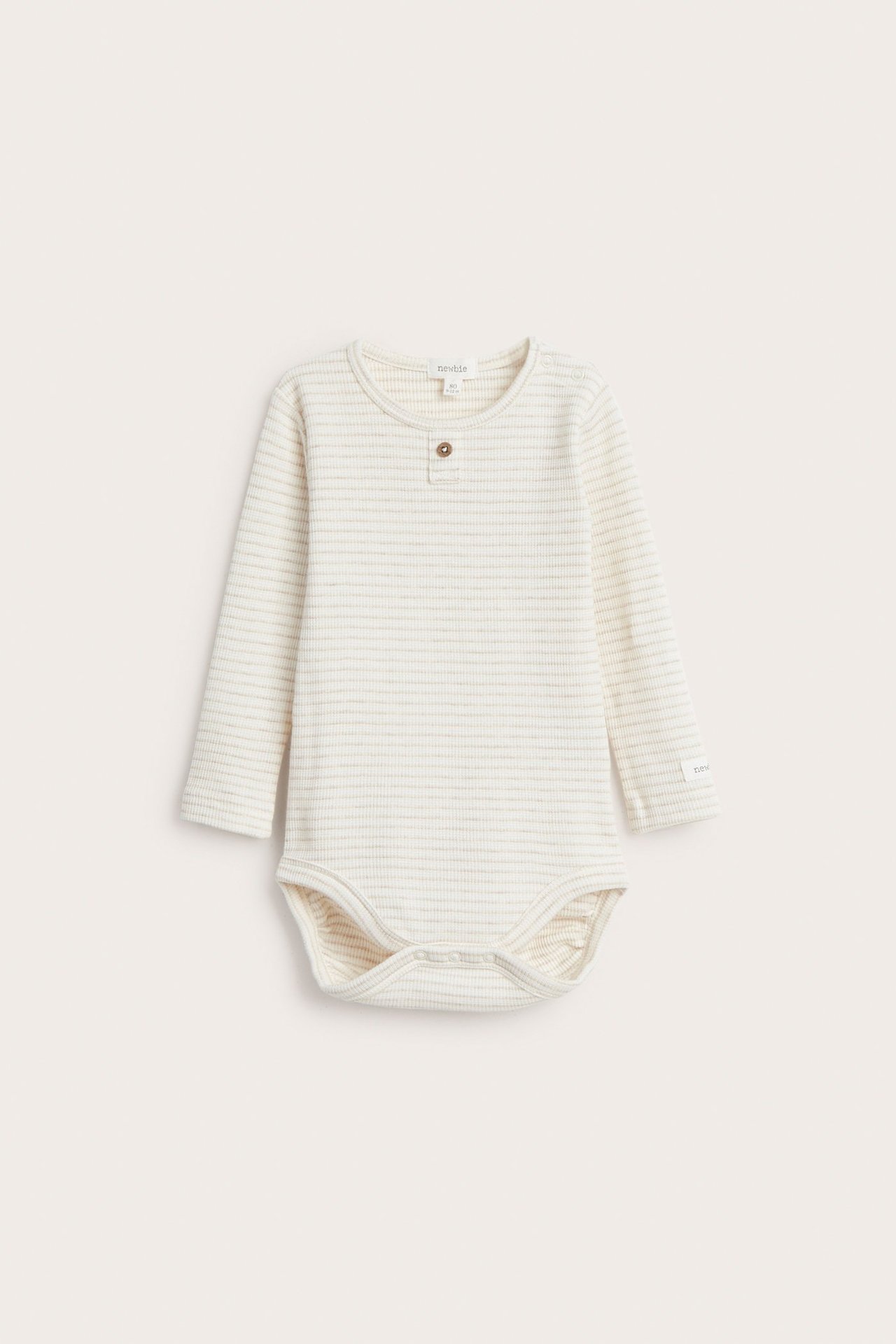 Edestä näkymä vauvan pitkähihaisesta beige melange raidallisesta vohvelibodysta neppareilla.