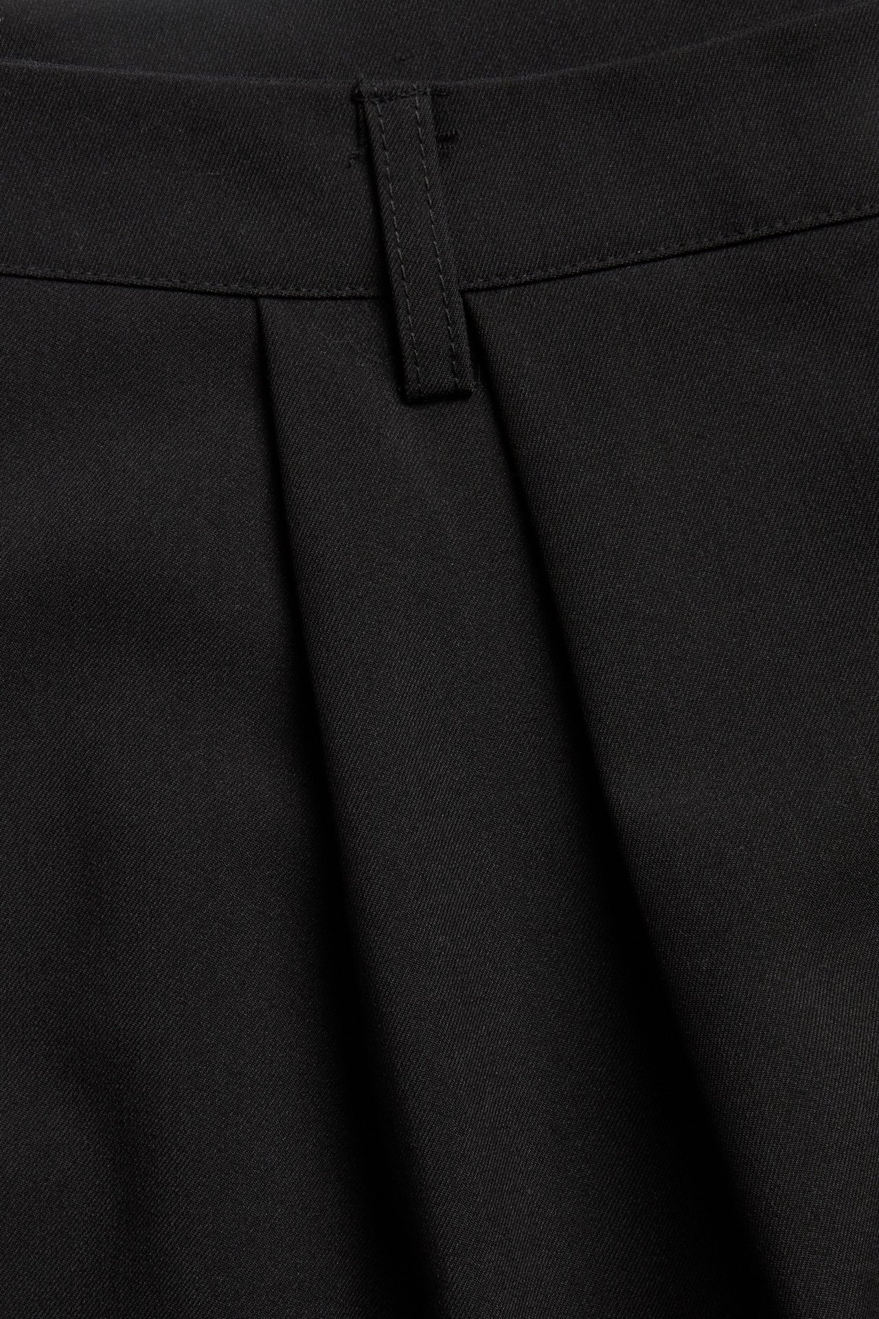 Zbliżenie czarnych spodni garniturowych z zakładkami i paskiem.