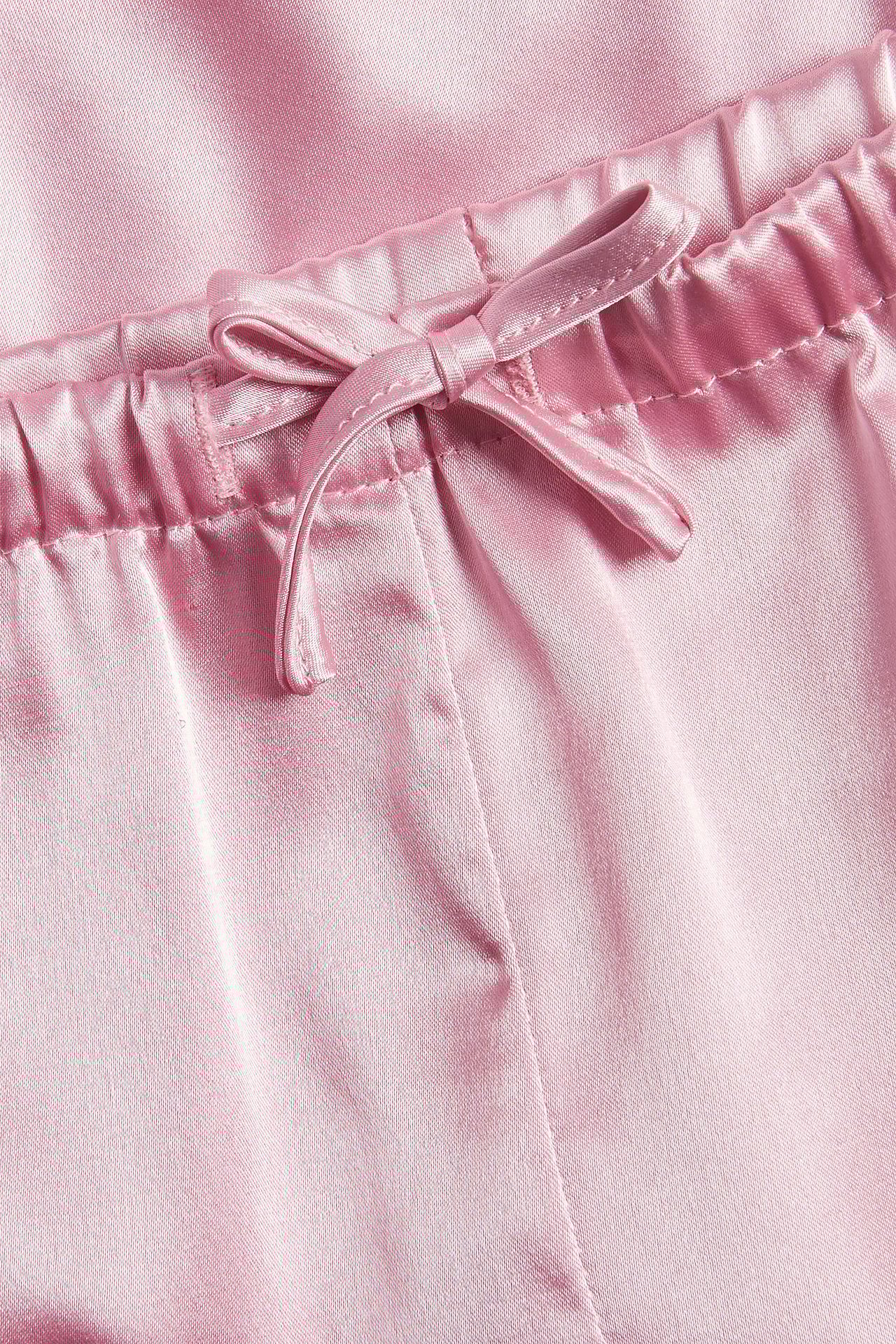 Närbild av ljusrosa pyjamasshorts i satin med resår och dragsko knuten i rosett.