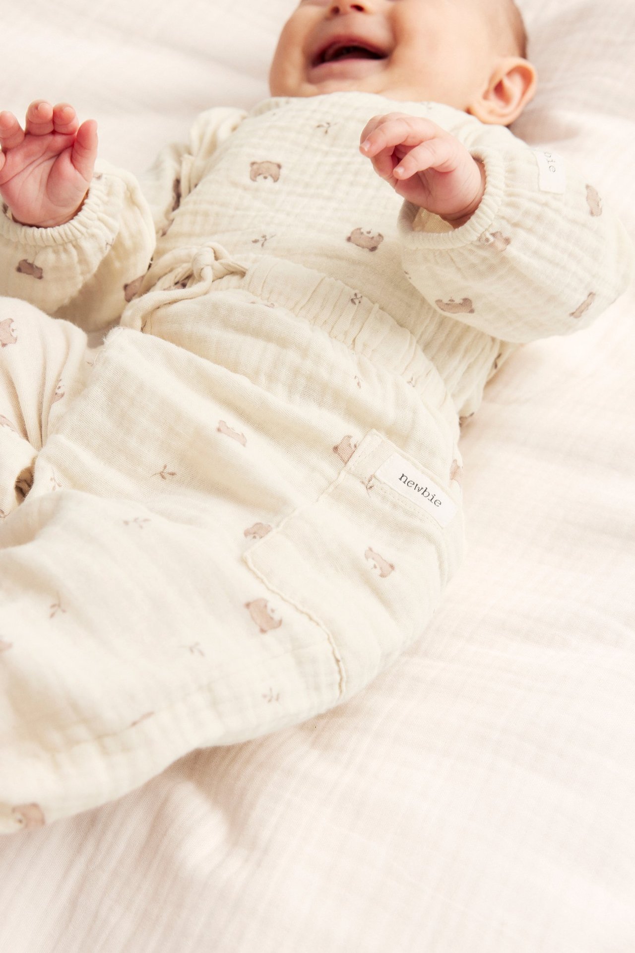 Närbild på baby i ljusbeige bomullsmuslinbyxor med björnmönster och matchande långärmad topp.