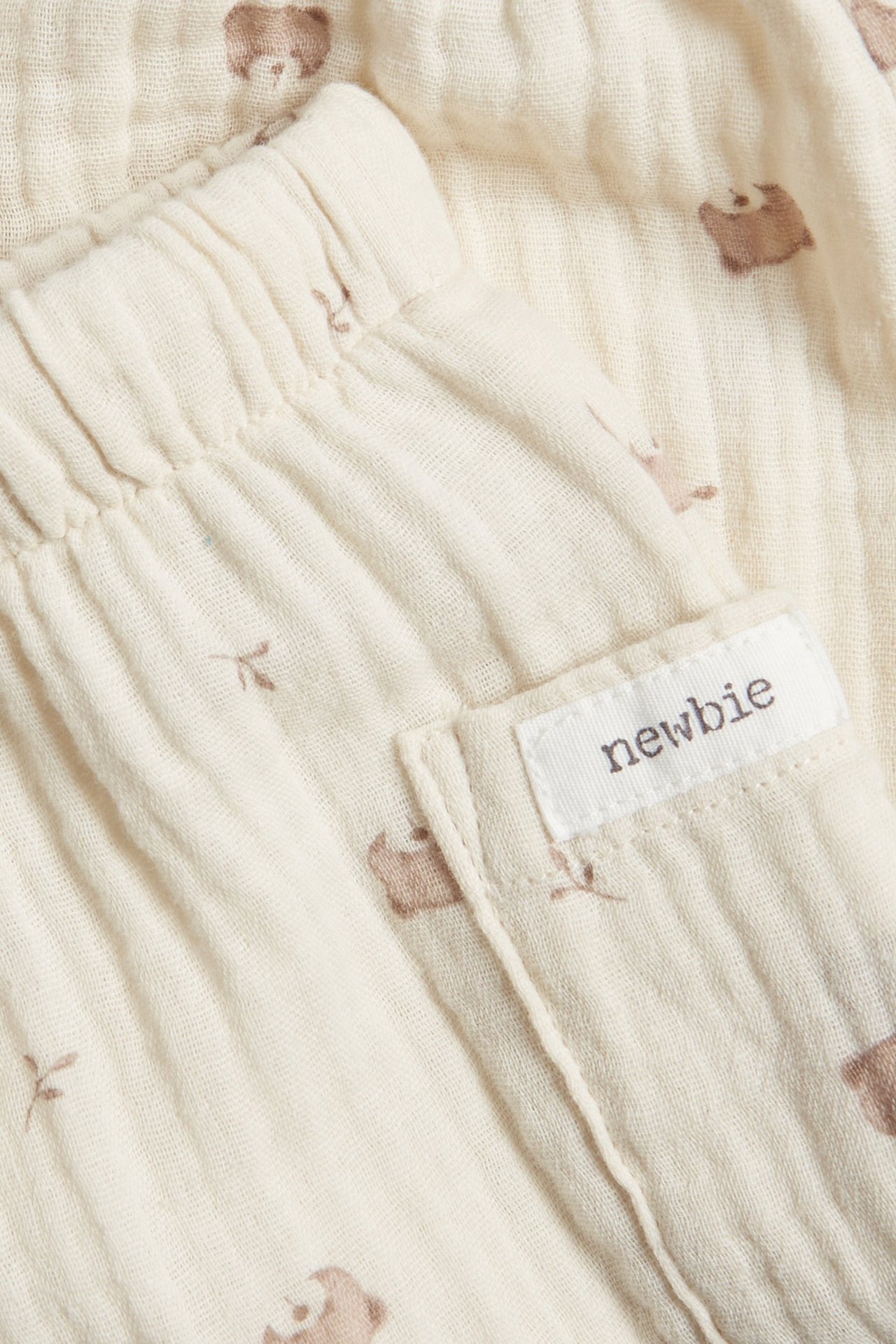 Zbliżenie jasnobeżowych muślinowych spodni niemowlęcych z elastyczną talią, kieszenią i brązowym wzorem.