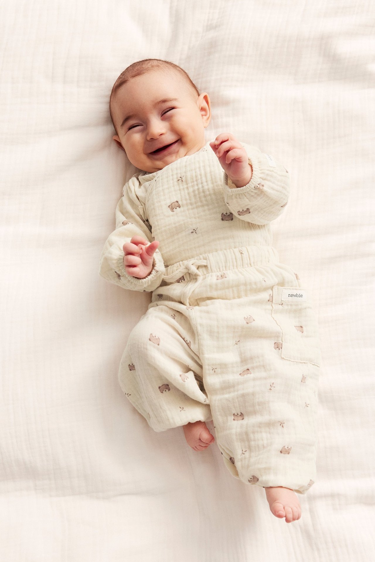 Uppifrån-vy av en leende baby i ljusbeige bomullsmuslinbyxor med djurmönster och matchande långärmad body.