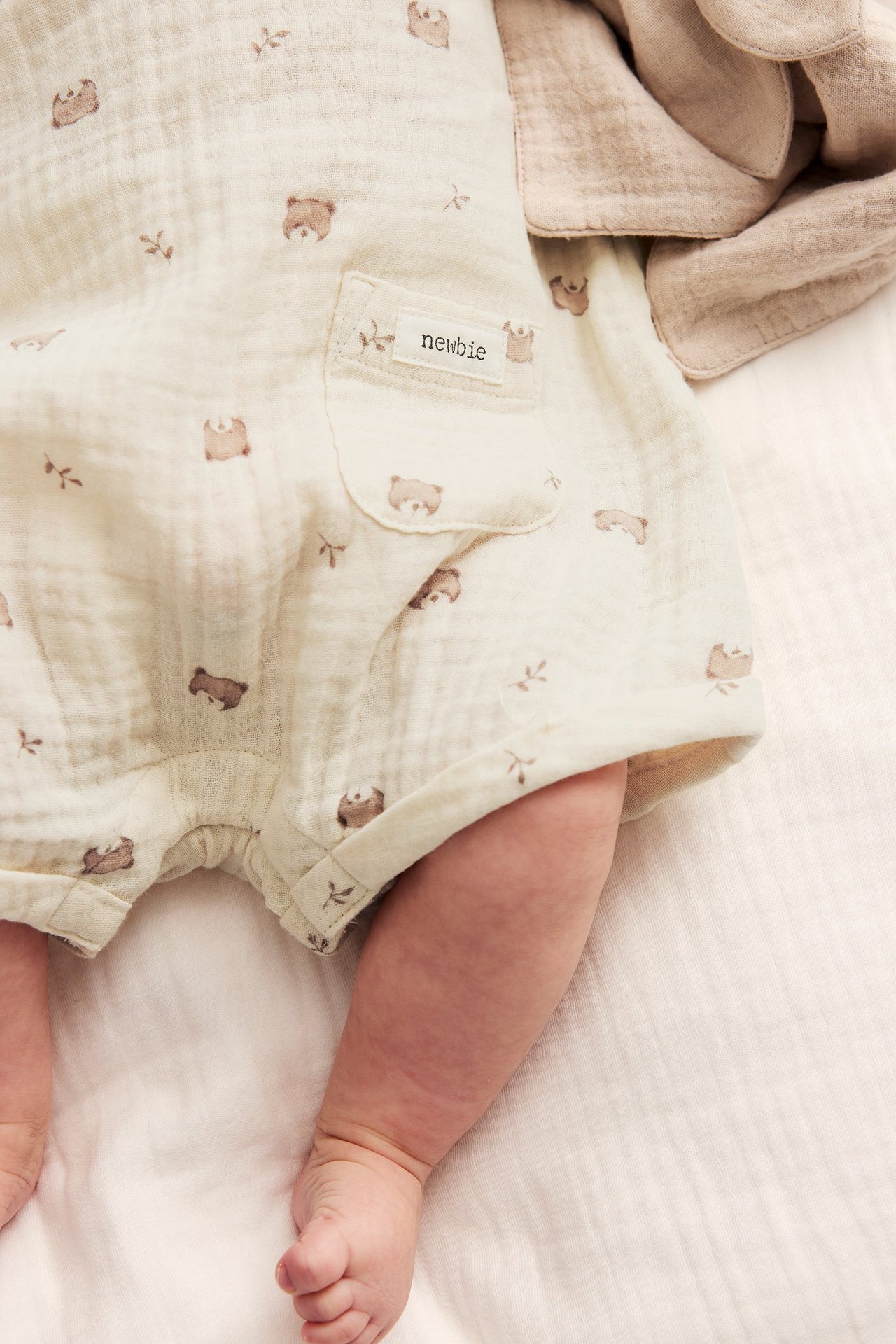 Närbild på en baby i en ljusbeige bomullsplaysuit med brunt nallemönster och framficka.