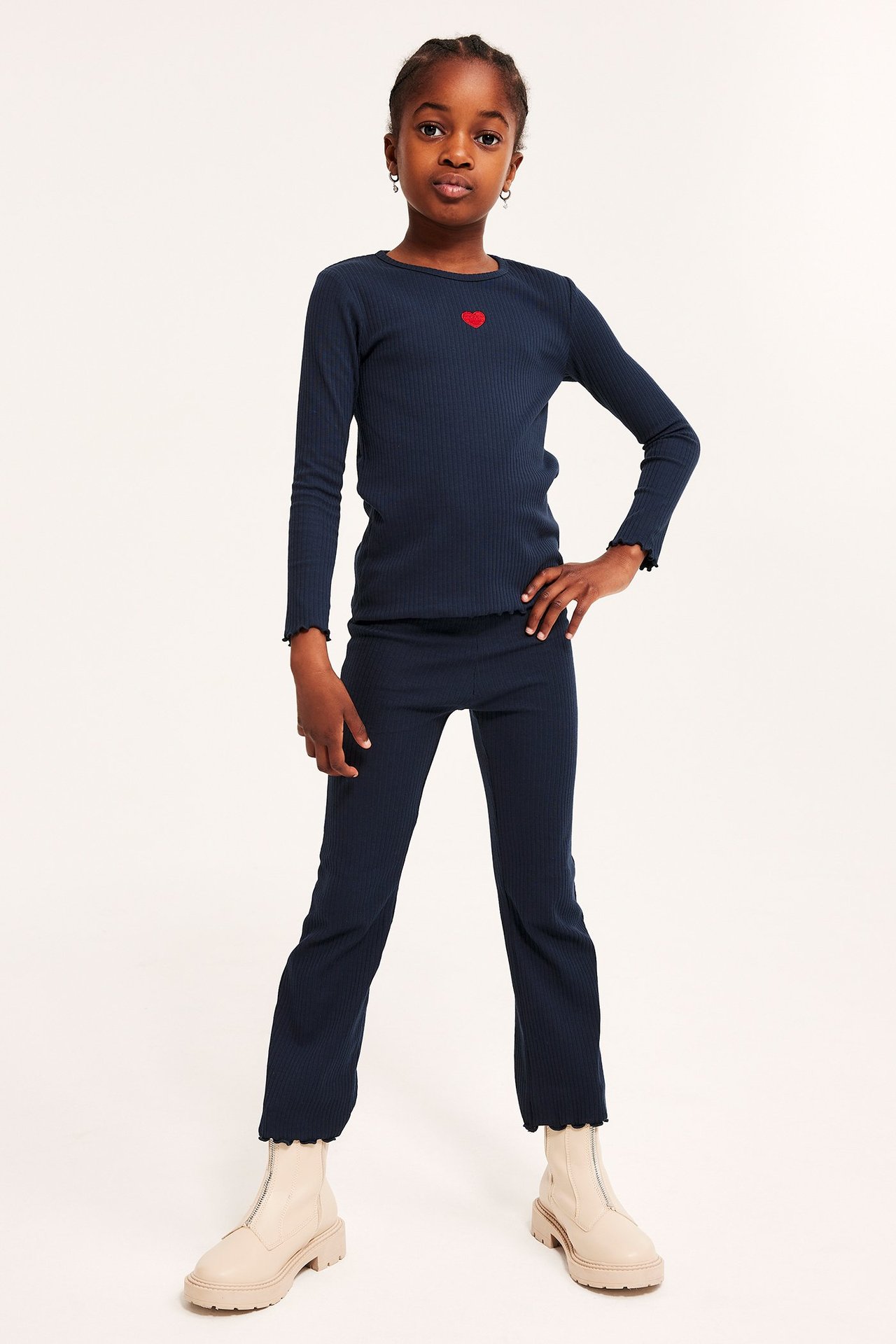 Frontvisning: Barn i mørkeblå ribbet langermet topp med rødt hjerte, matchende bukser og beige støvler.
