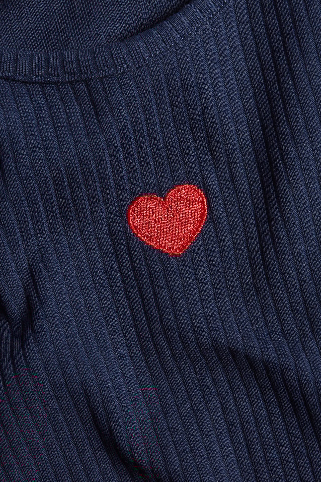 Zbliżenie na granatowy prążkowany top z długim rękawem i czerwonym haftowanym sercem.