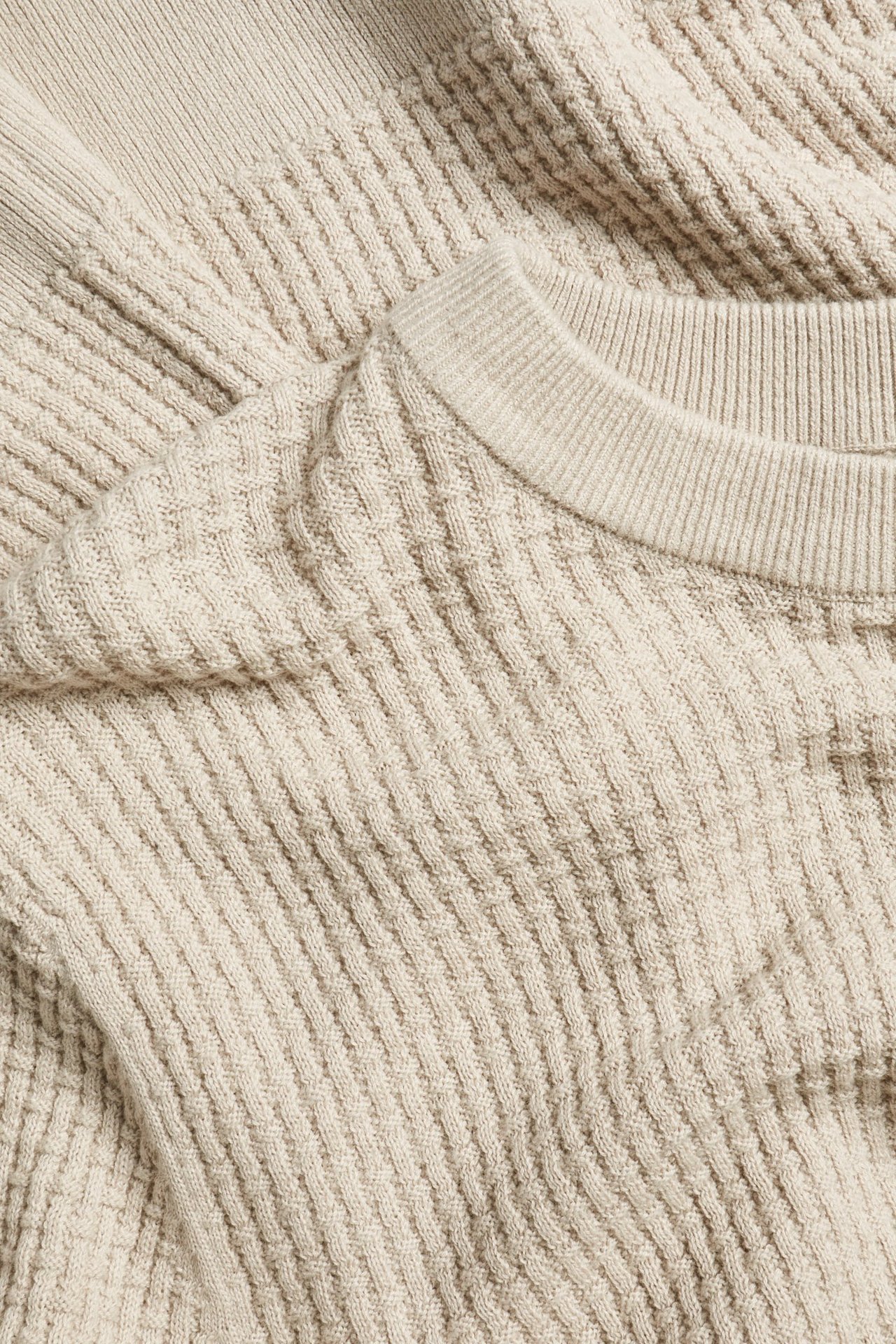 Zbliżenie na jasnobeżowy bawełniany sweter z okrągłym dekoltem i wzorzystym splotem.