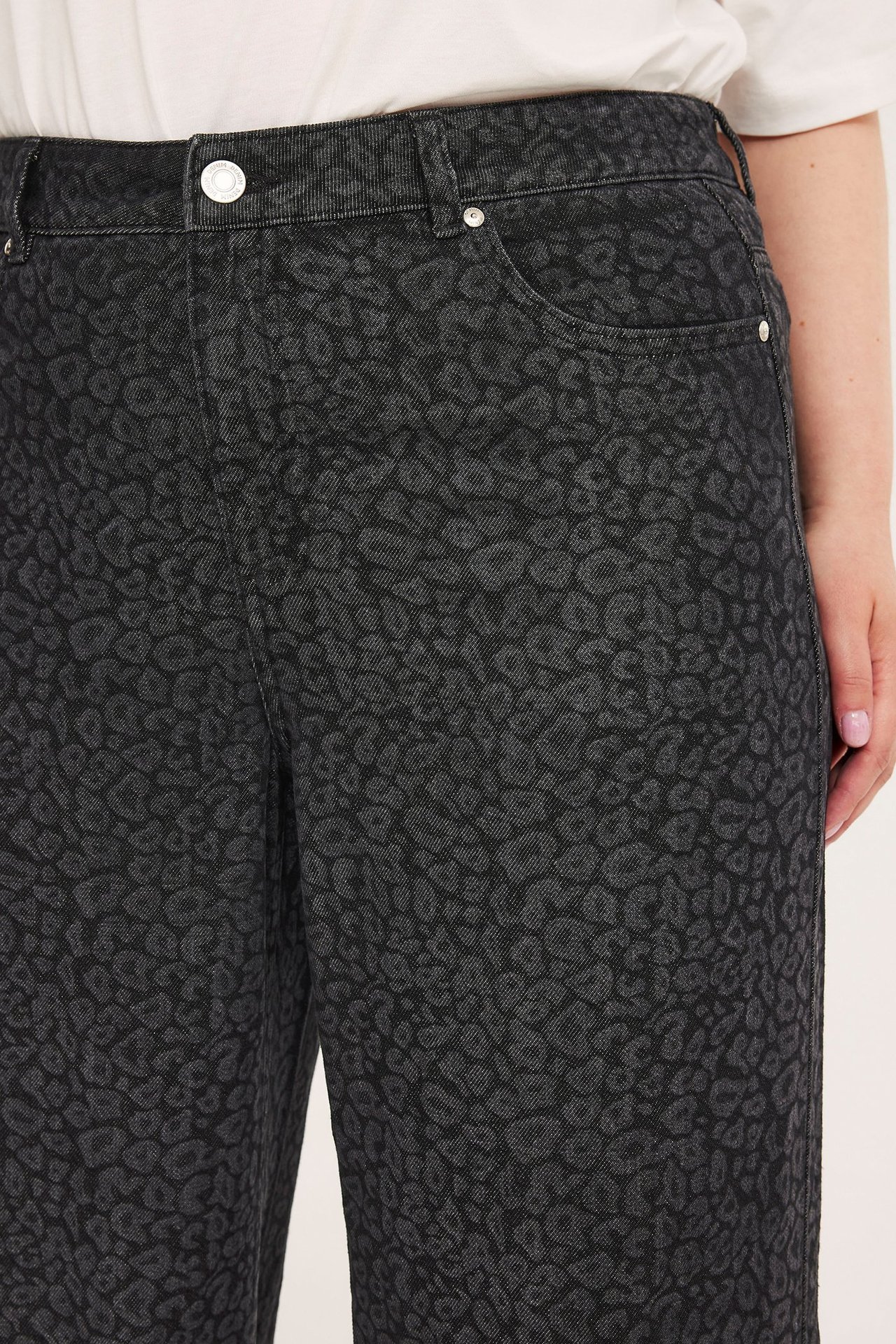 Närbild framifrån av kvinnas gråa leopardmönstrade, höga, vida jeans, stylade med en vit topp.