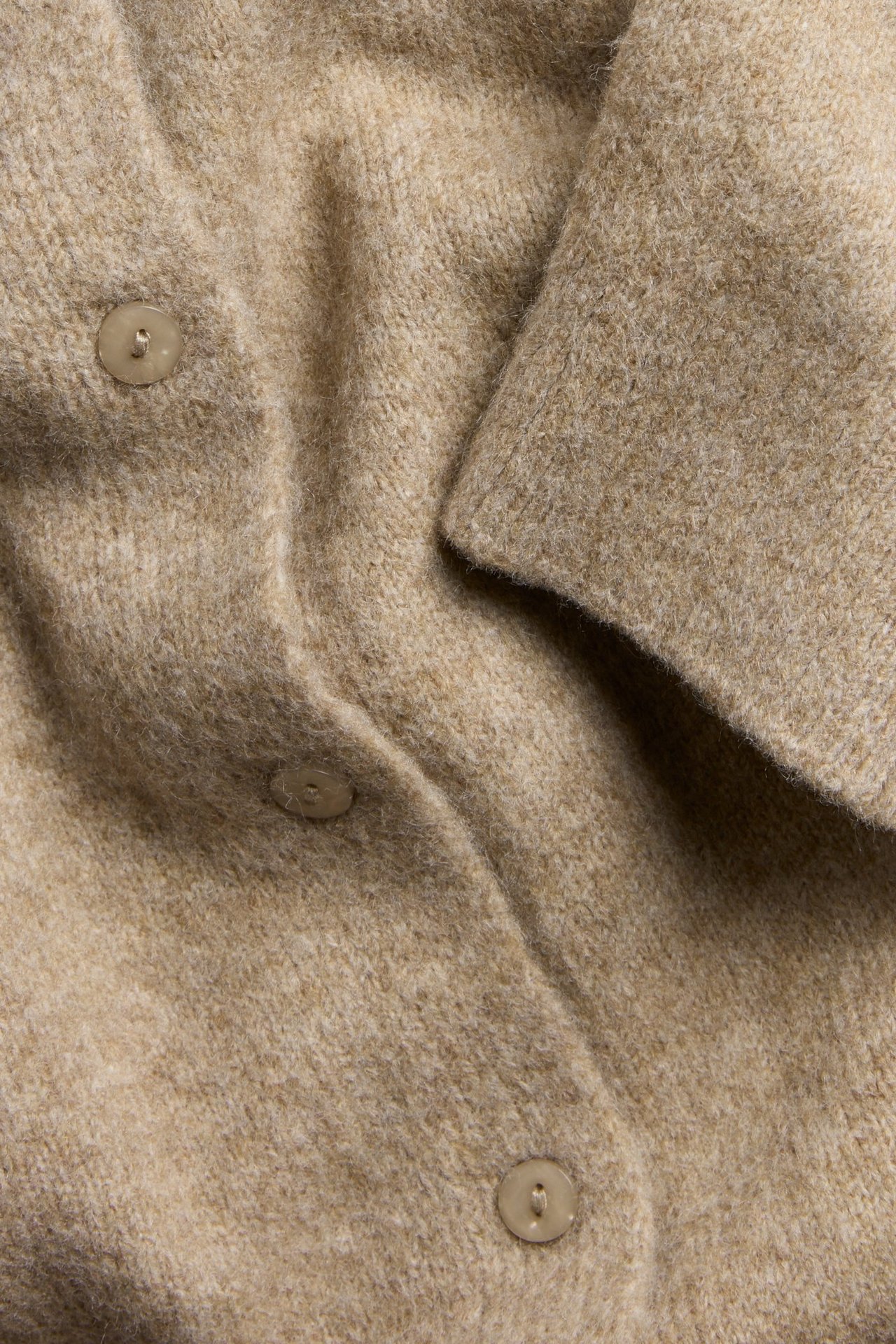 Zbliżenie na brązowy melanżowy dzianinowy kardigan z krótkim rękawem i widocznymi guzikami.