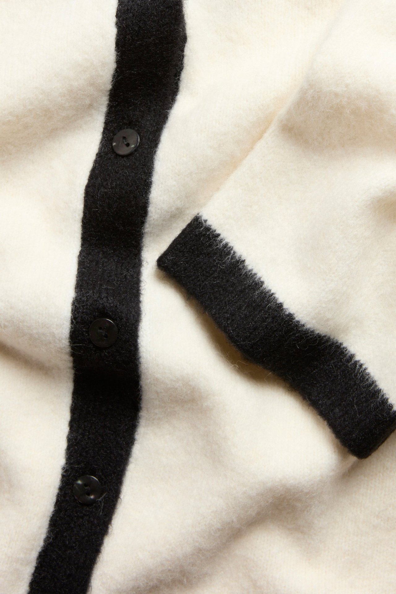 Zbliżenie na kremowy melanżowy kardigan z krótkim rękawem, z czarnymi paskami i guzikami.