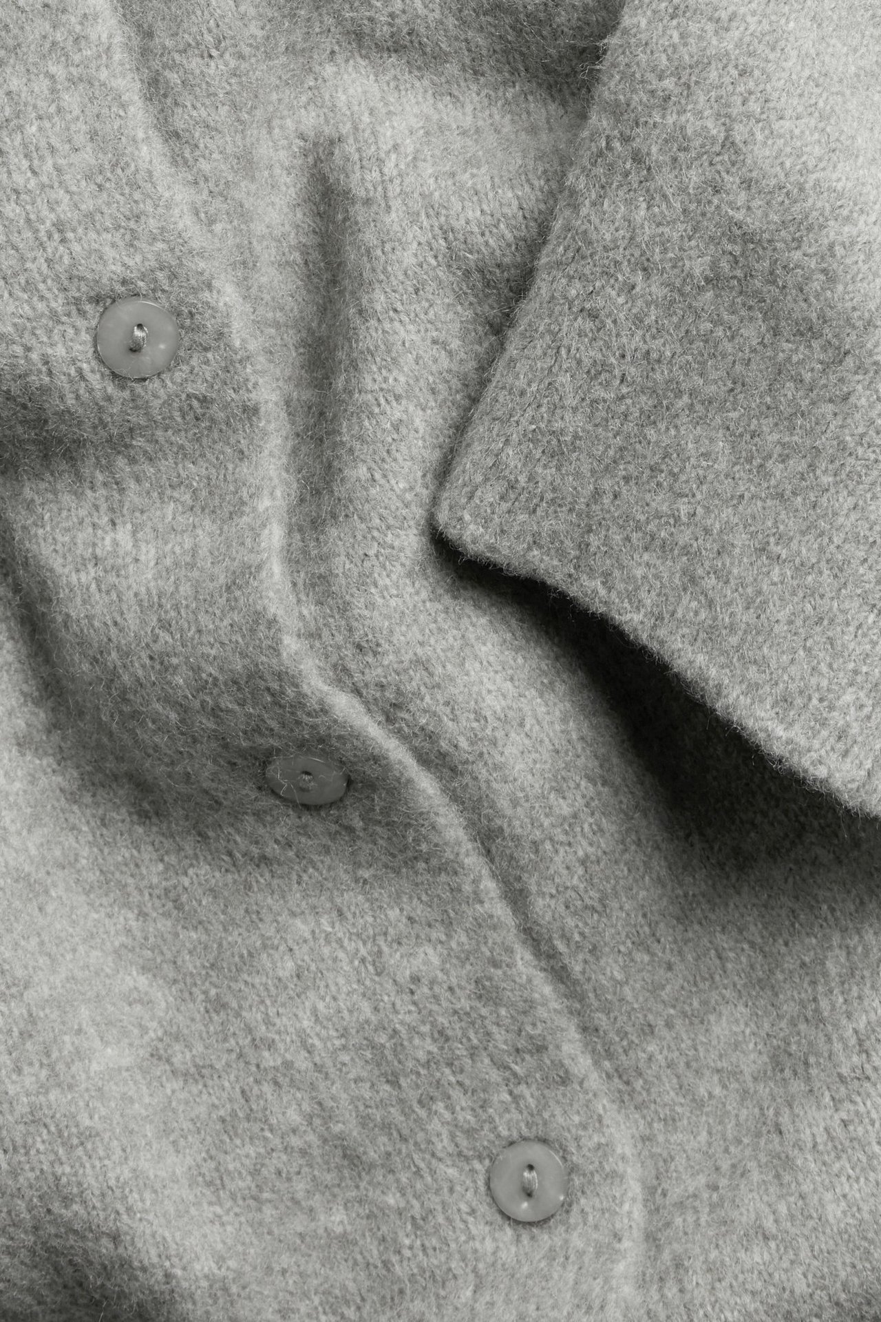 Zbliżenie jasnoszarego melanżowego, dzianinowego, krótkiego kardiganu z guzikami.