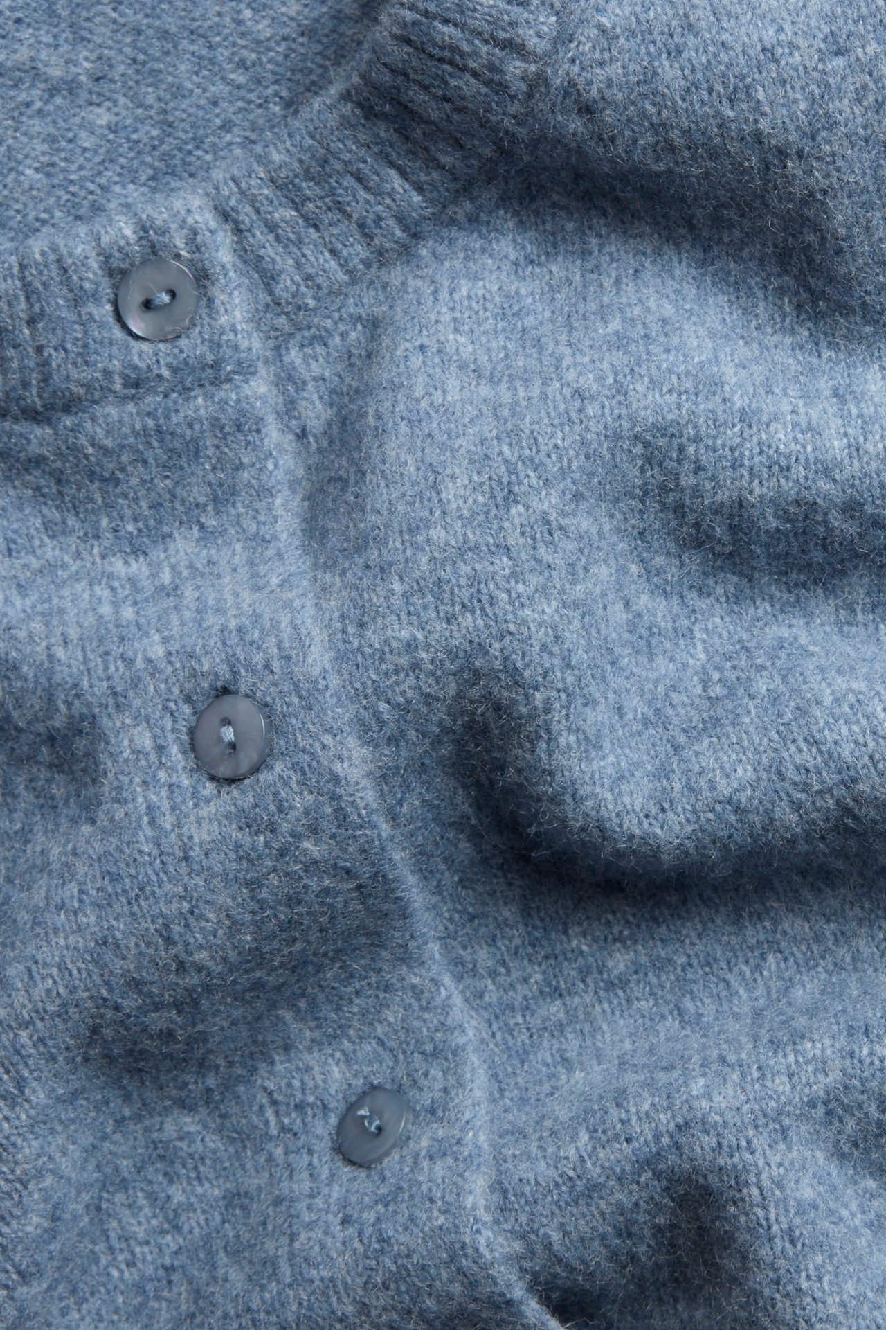 Zbliżenie na jasnoniebieski melanżowy sweter rozpinany z trzema widocznymi guzikami.